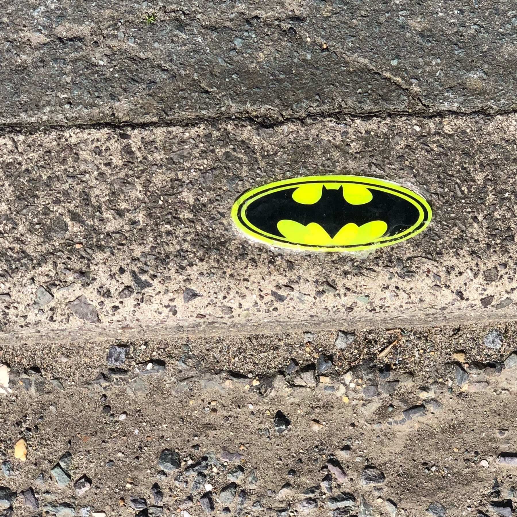 A batman logo sticker on a kerb. 