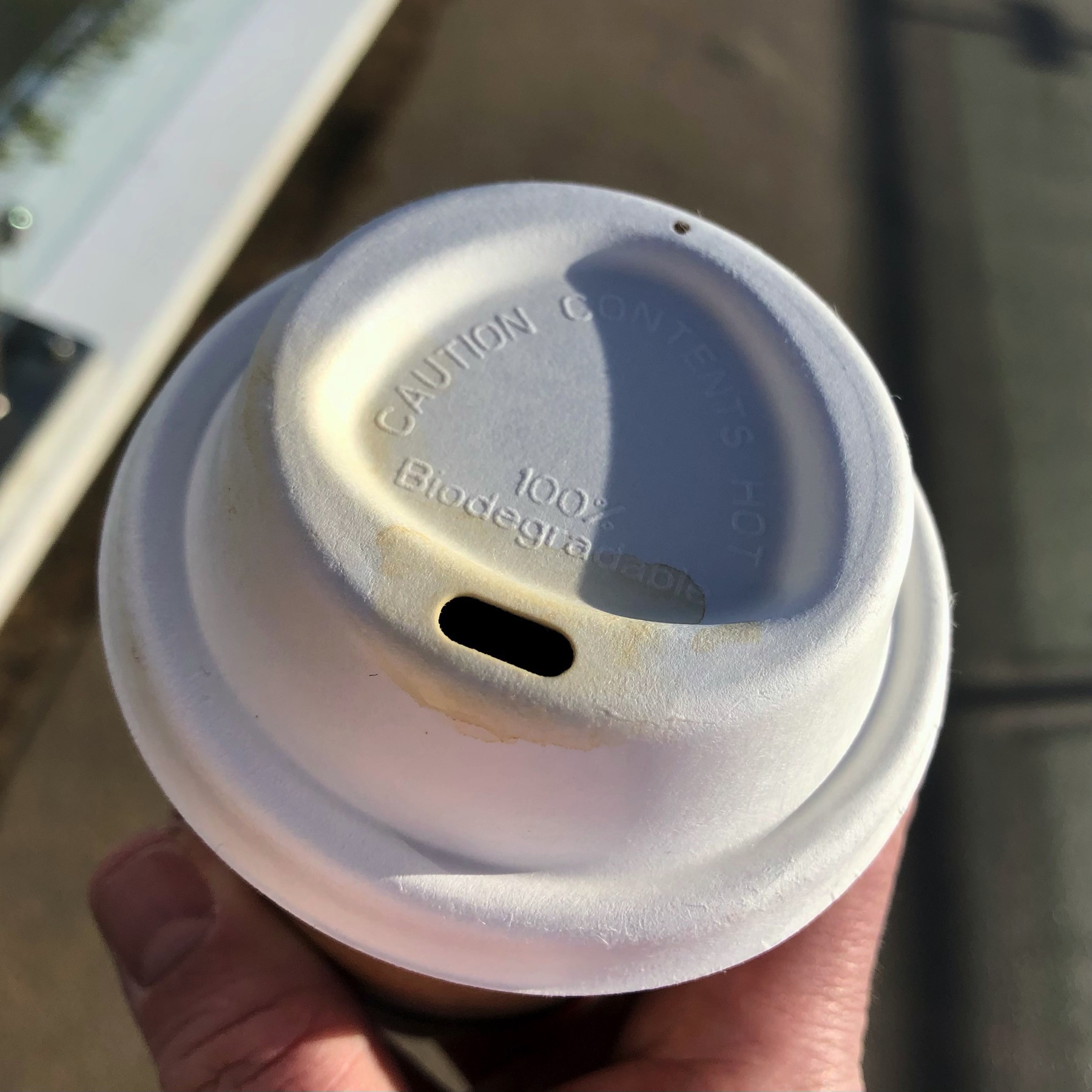 A biodegradable coffe cup lid, on a coffee, in a man’s hand. 