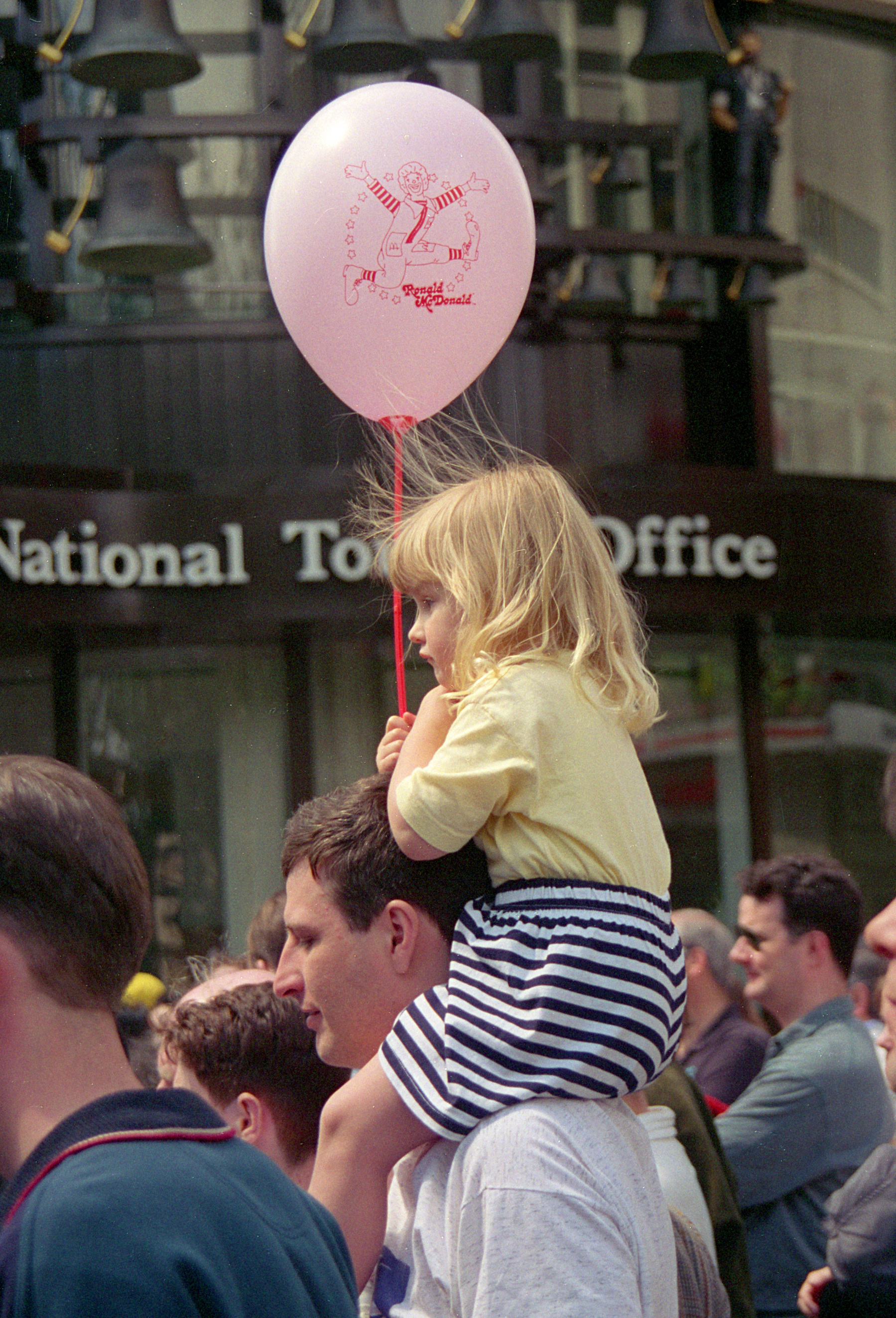 A girl cluching a Ronald McDonald ballon on her father’s shoulders, near the Swiss Centre in Leicester Square — 1994. 