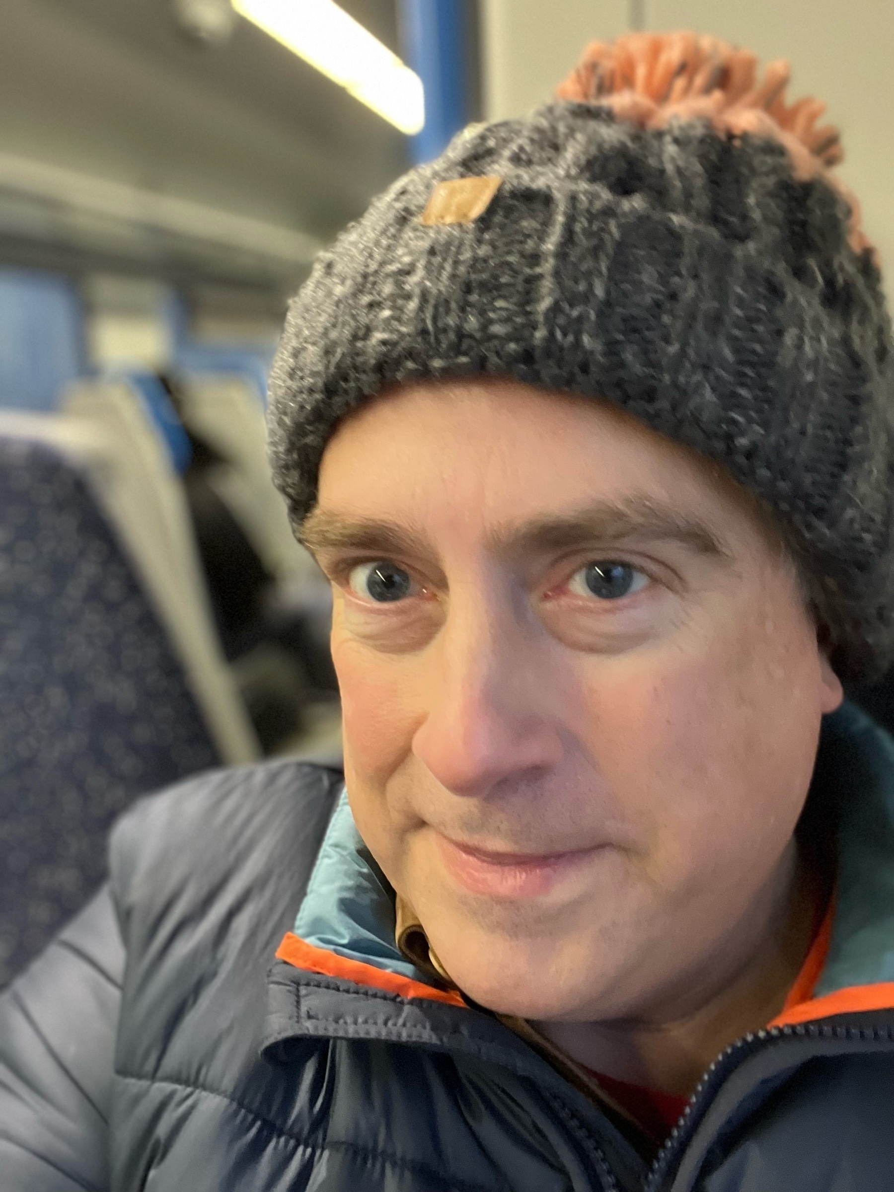 Adam on a train, wearing a woolly hat. 