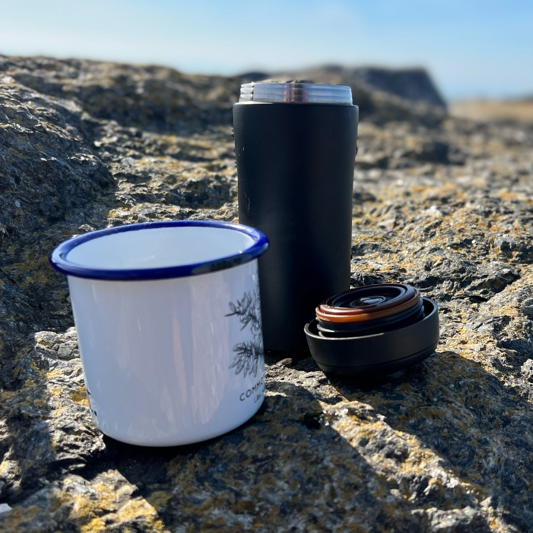 A flask and enamel mug on a rock.
