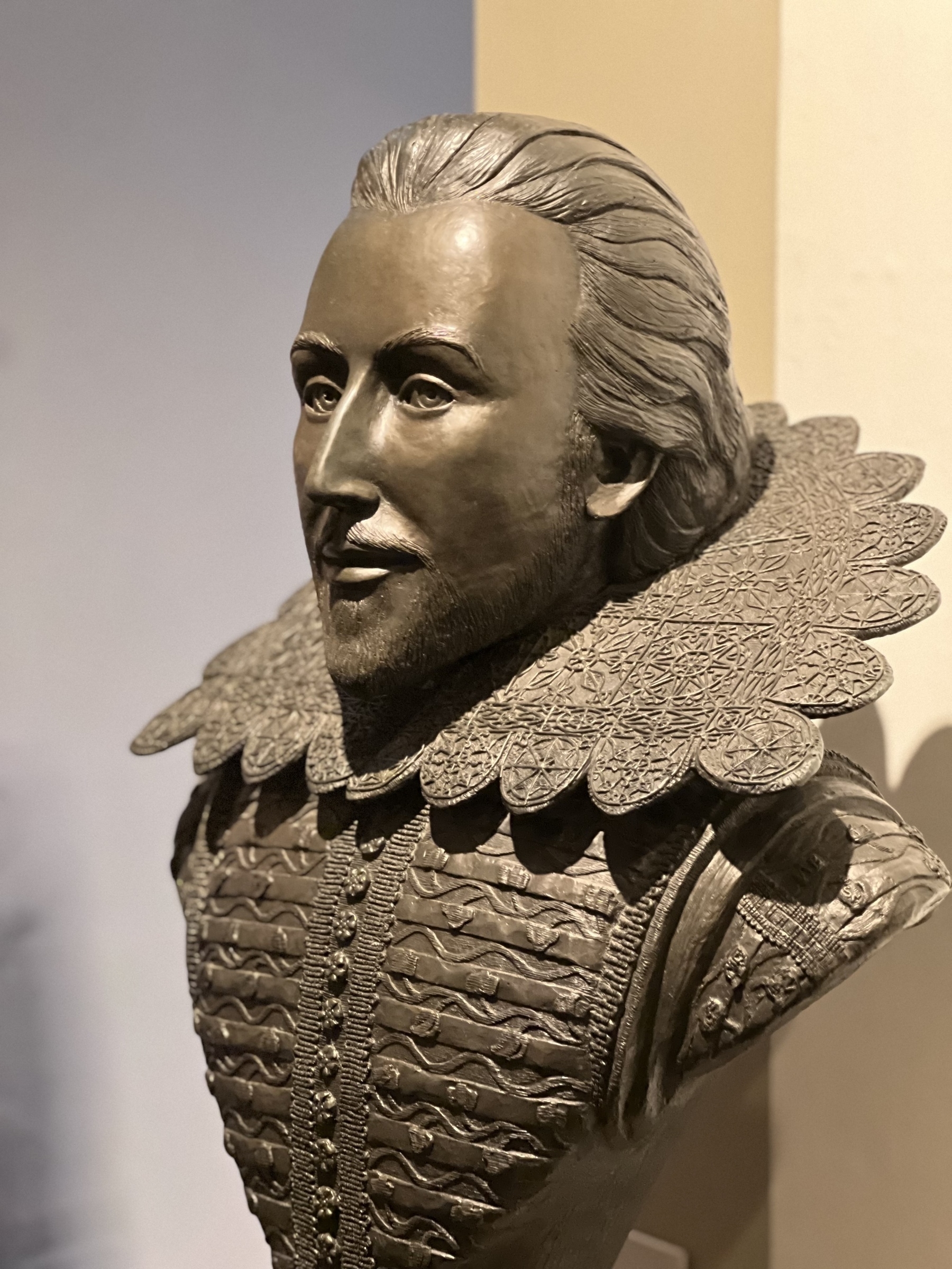 A detailed bronze bust portrays William Shakespeare dressed in ornate clothing typical of the Renaissance period.