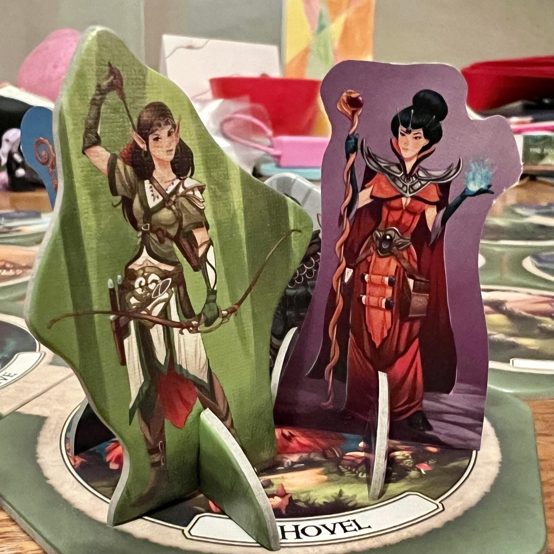 Two standee figures of fantasy characters, one in armor with a sword and the other in a robe holding a staff, are placed on a board game setting.