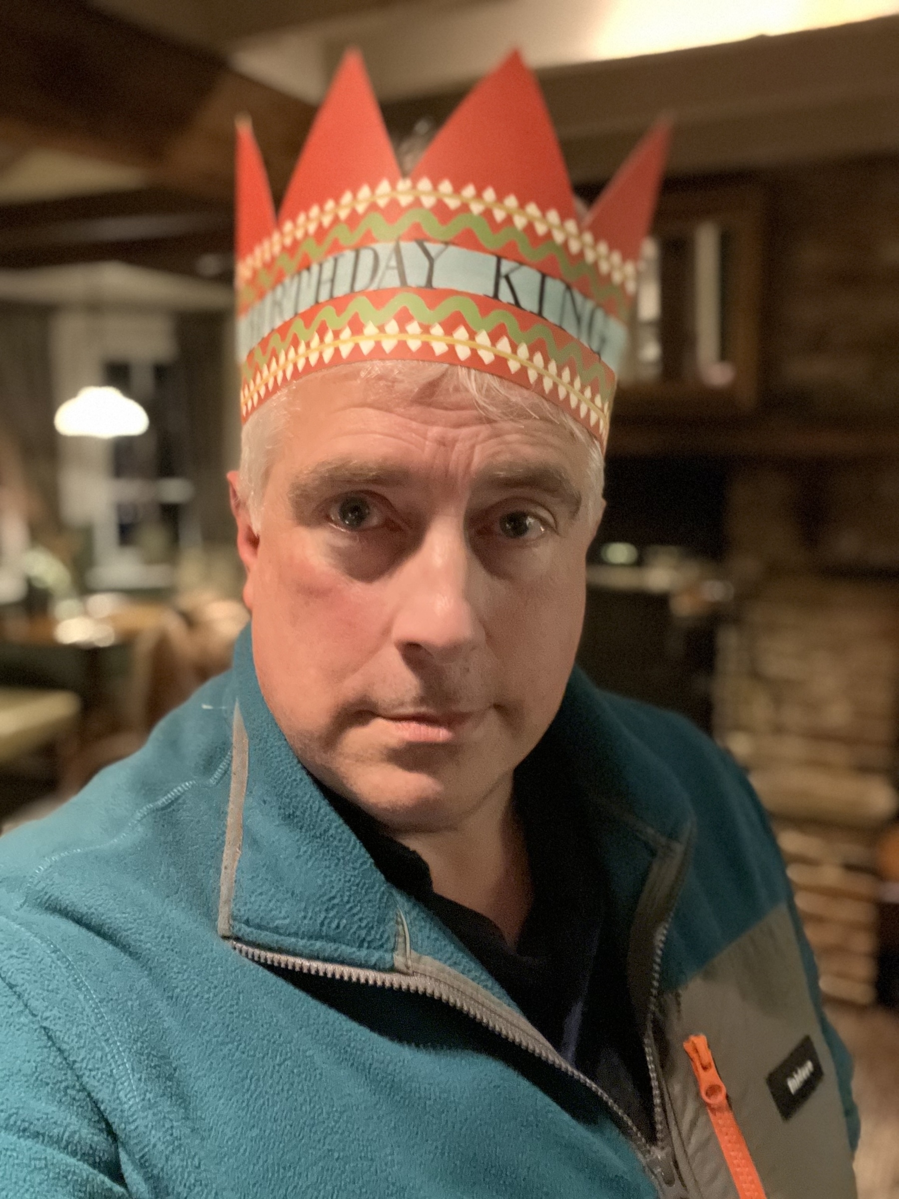 Adam Tinworth wearing a paper crown labeled "BIRTHDAY KING" poses for a photo in a pub.