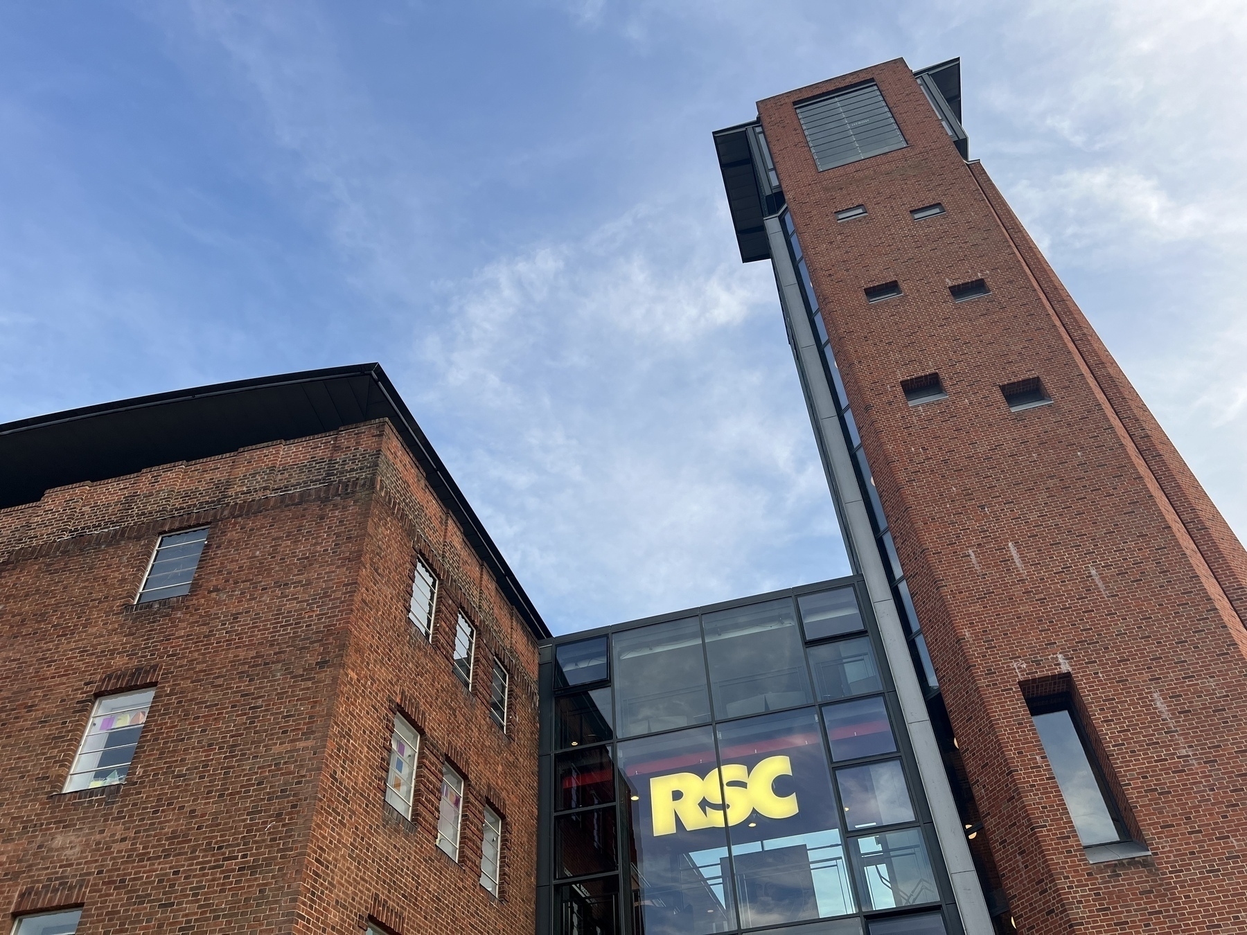 The Swan Theatre: A red brick building with a modern glass section displays large "RSC" signage against a backdrop of a clear sky.