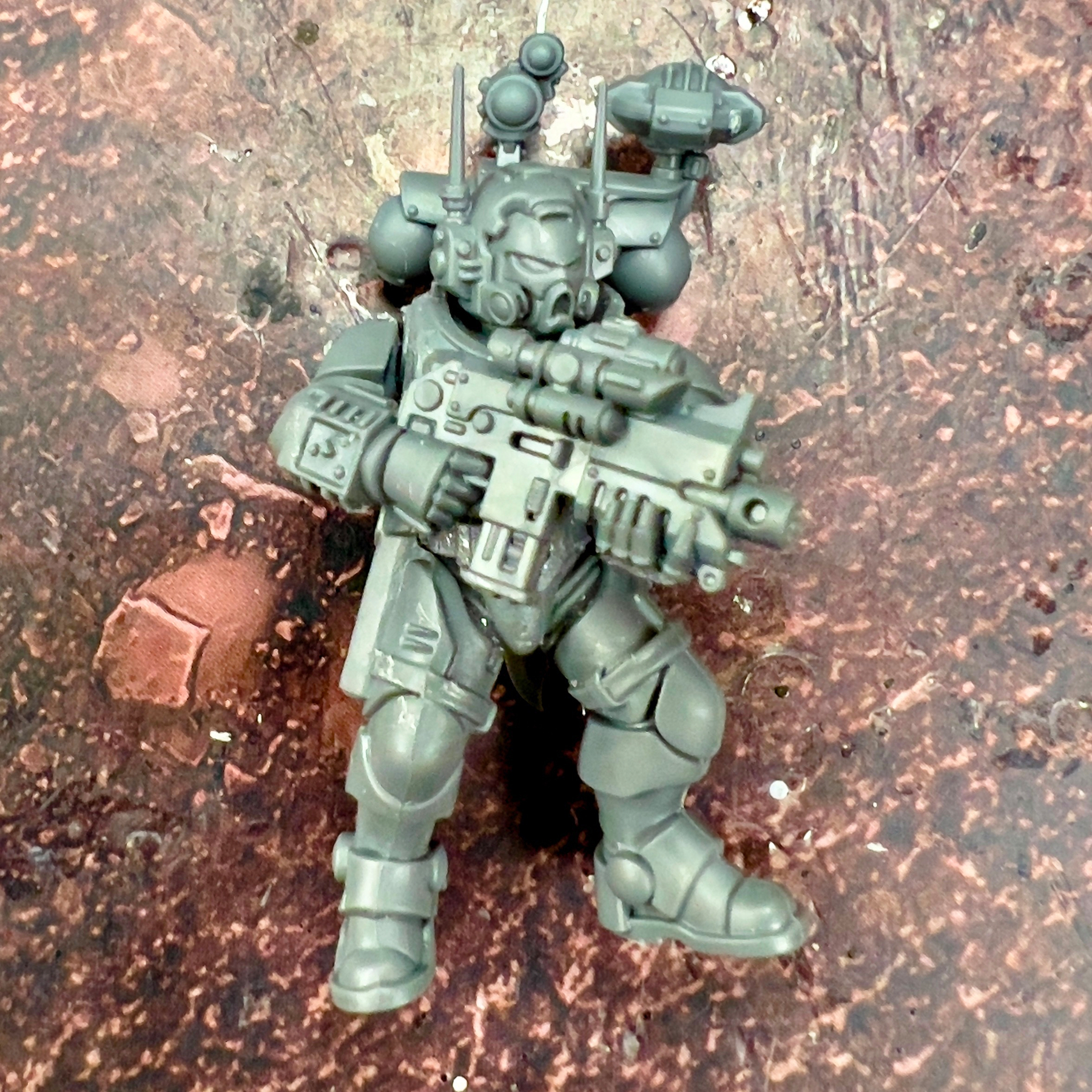 A sci-fi miniature figurine dressed in futuristic armor holds a large weapon against a textured background.