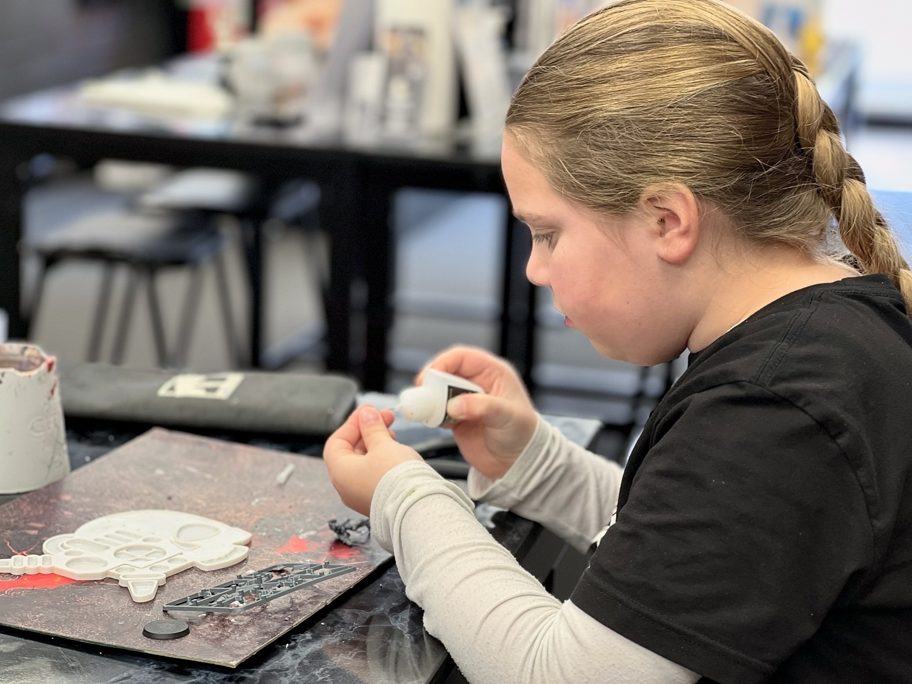 A child is engaged in assembling a Warhammer 40k miniature at a table, in a Warhammer shop.