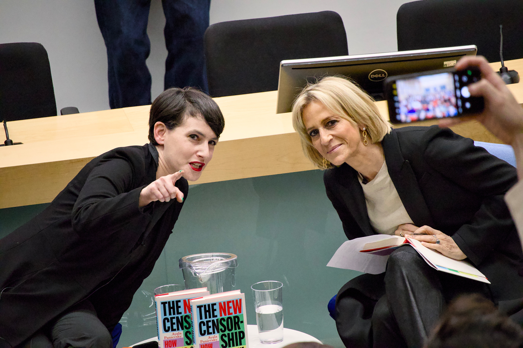Two people are sitting at a table with books titled The New Censorship, engaging in a discussion while someone takes a photo.