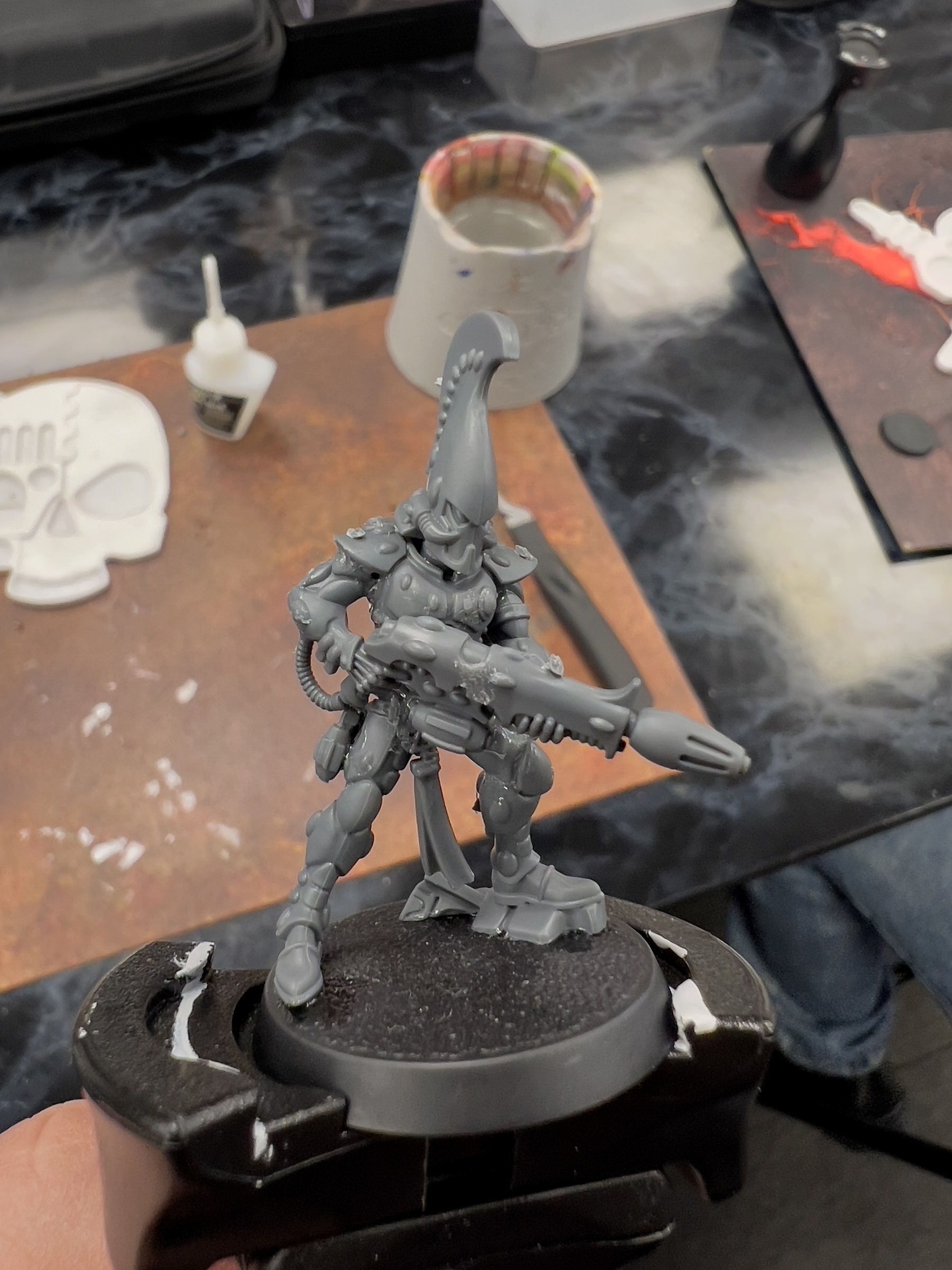 A detailed miniature figure of a futuristic armored soldier holding a weapon and wearing a helmet with an elongated crest is being assembled.