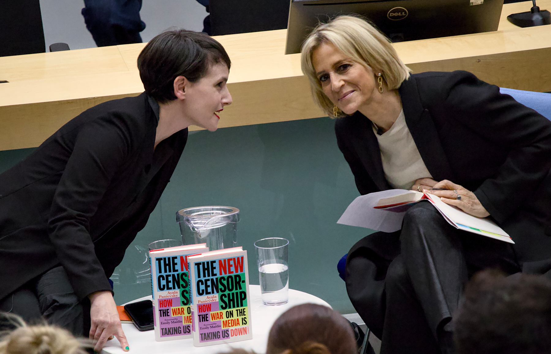 Two women are engaged in conversation at a seated event, with books titled The New Censorship on a table between them.