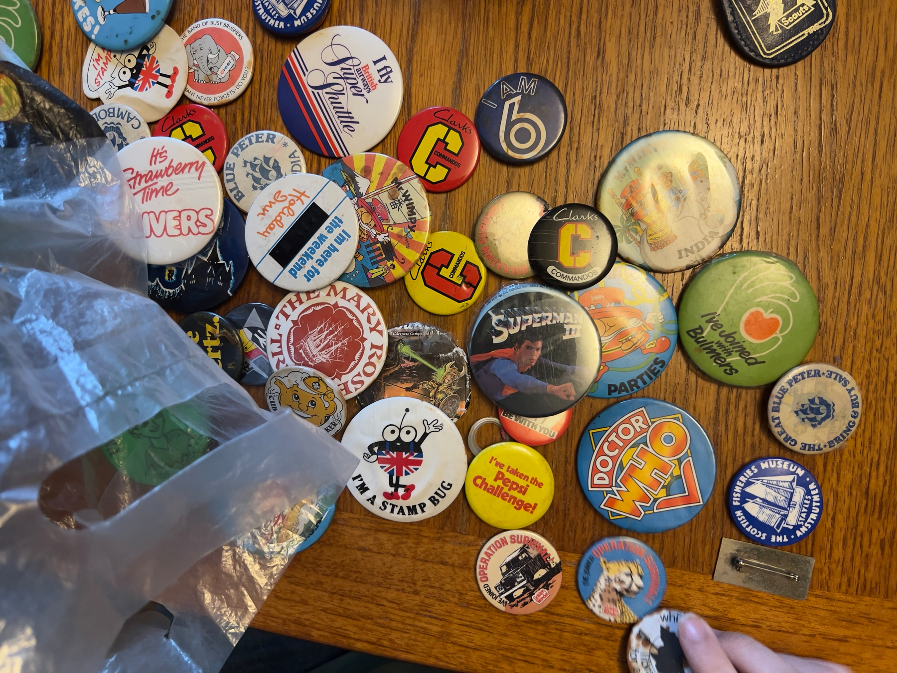 A collection of vintage pins and badges featuring various designs and logos is displayed on a wooden surface.