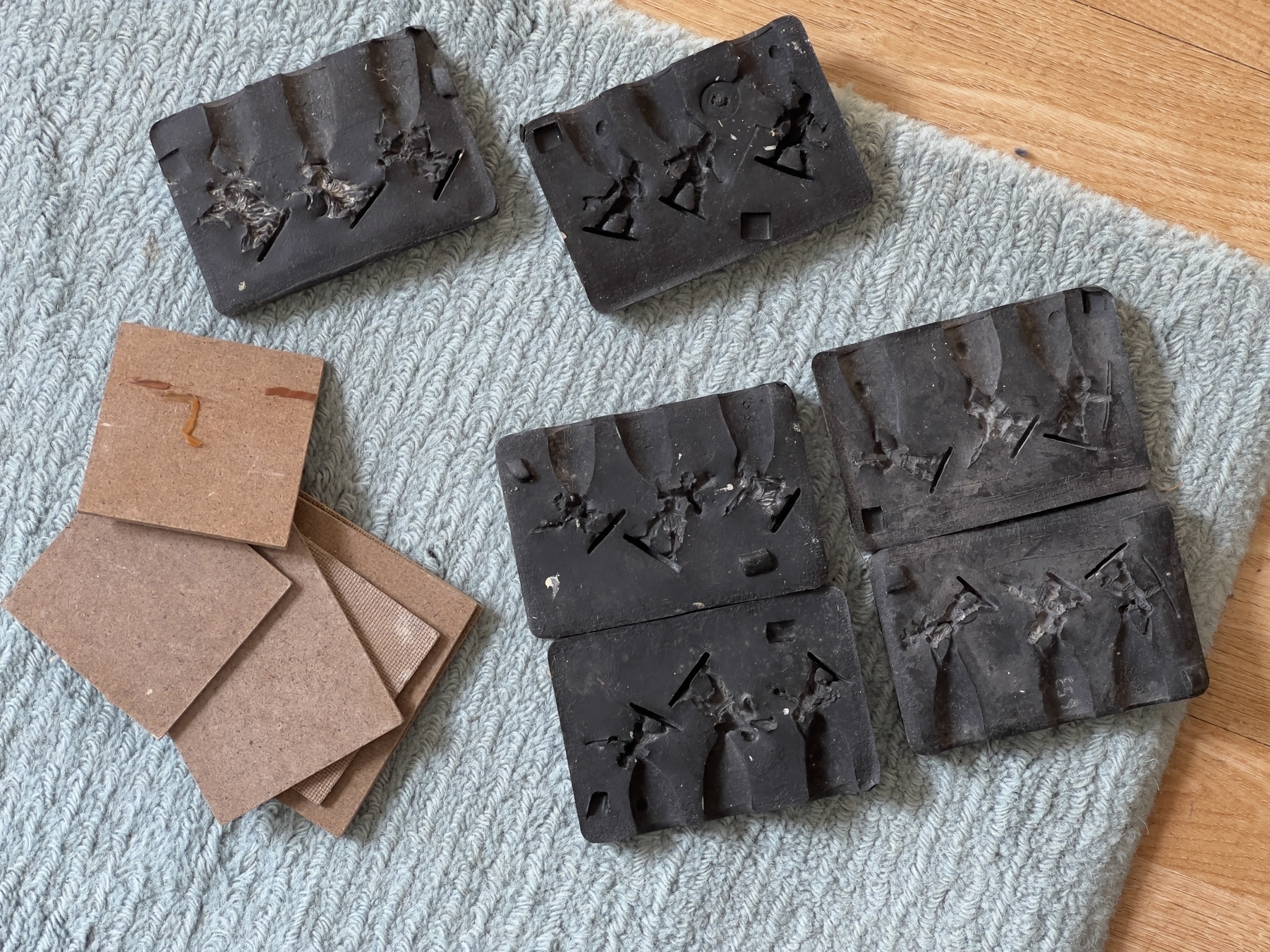 Black, rectangular rubber moulds with miniature figure patterns are placed alongside some brown paper cards on a textured surface.