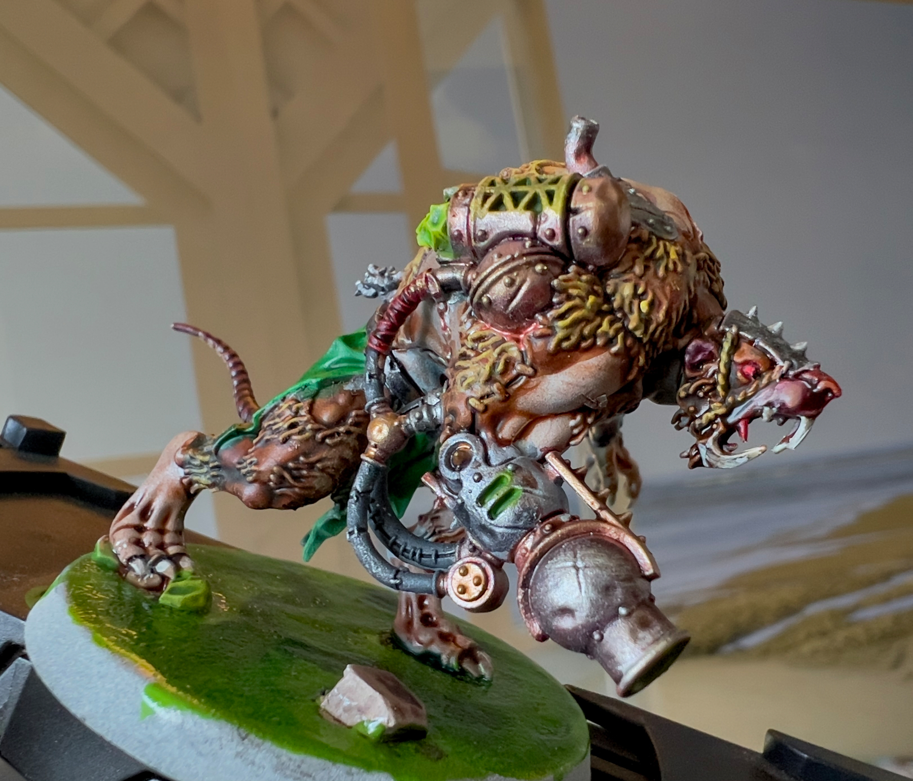 A detailed miniature model of a mechanical, rat-like creature with intricate steampunk elements and a green cloak is mounted on a circular base.