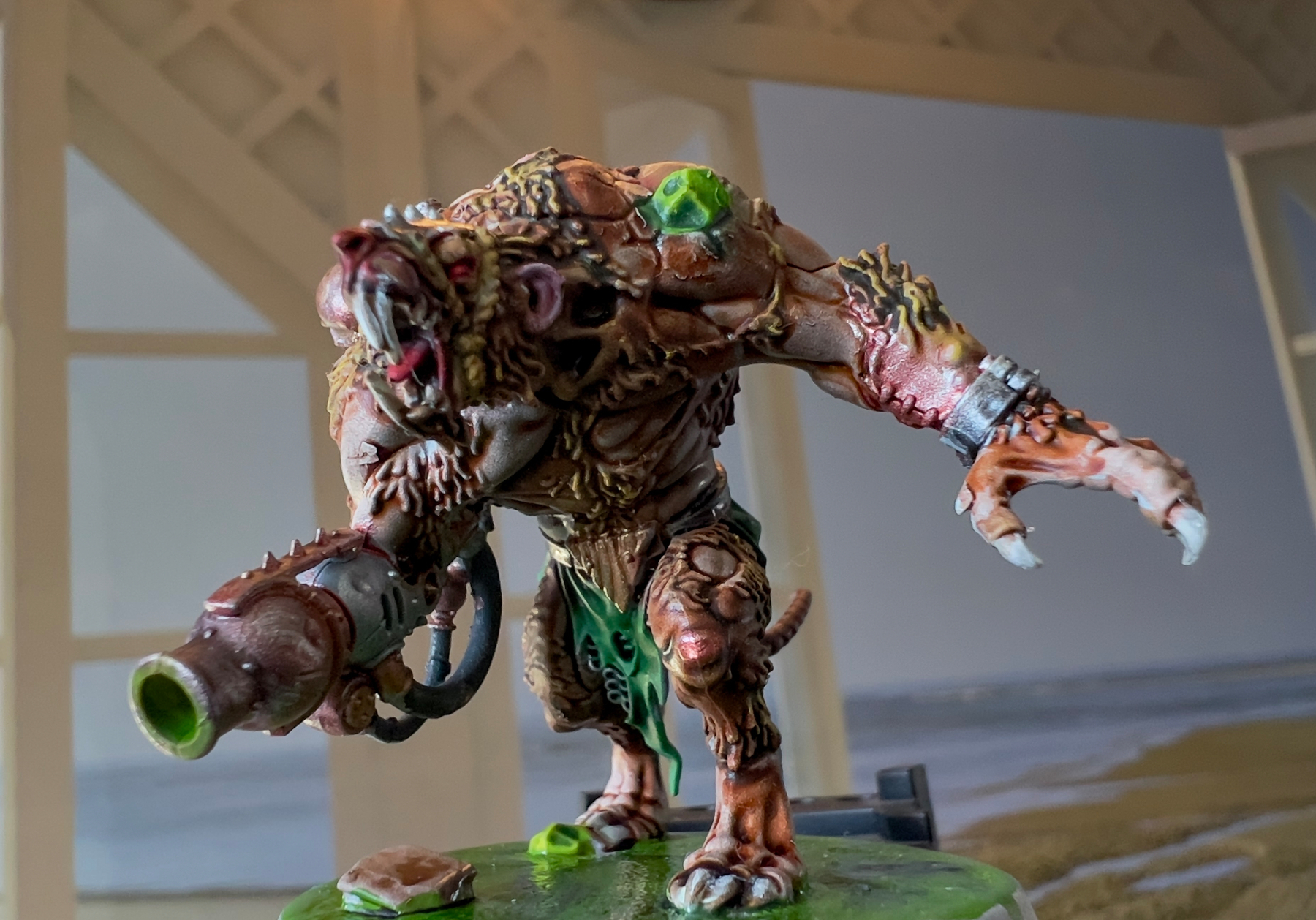 A detailed model of a mutant creature with mechanical elements and a large weapon stands in a dynamic pose against a blurred background.