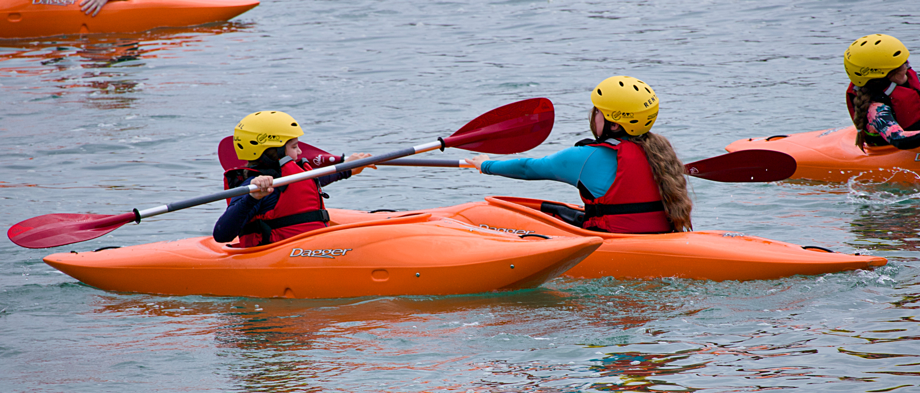 People wearing helmets and life vests are kayaking on a body of water.