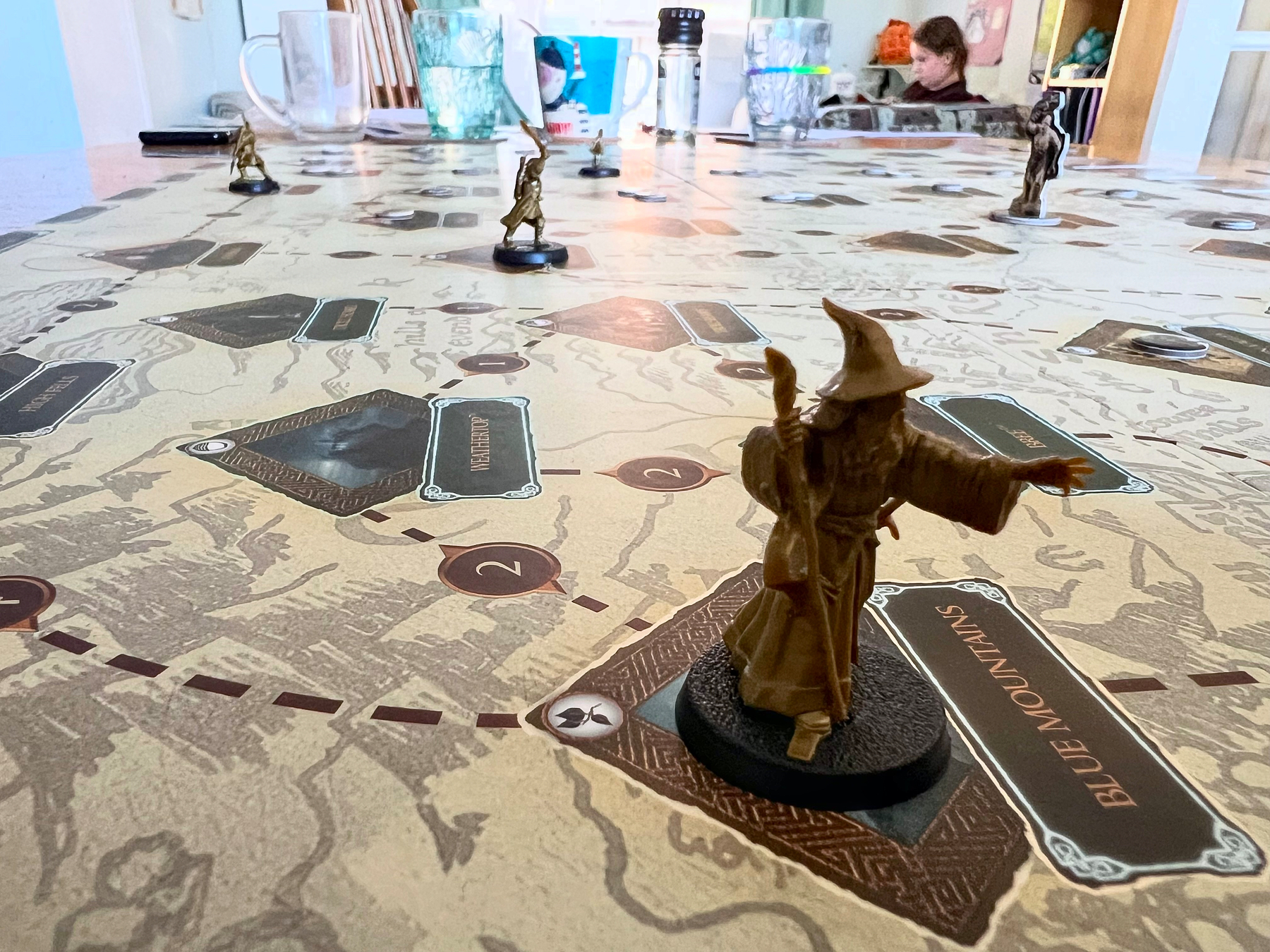 A tabletop game featuring detailed character miniatures is set up on a map with various labeled locations, including one marked Blue Mountain.