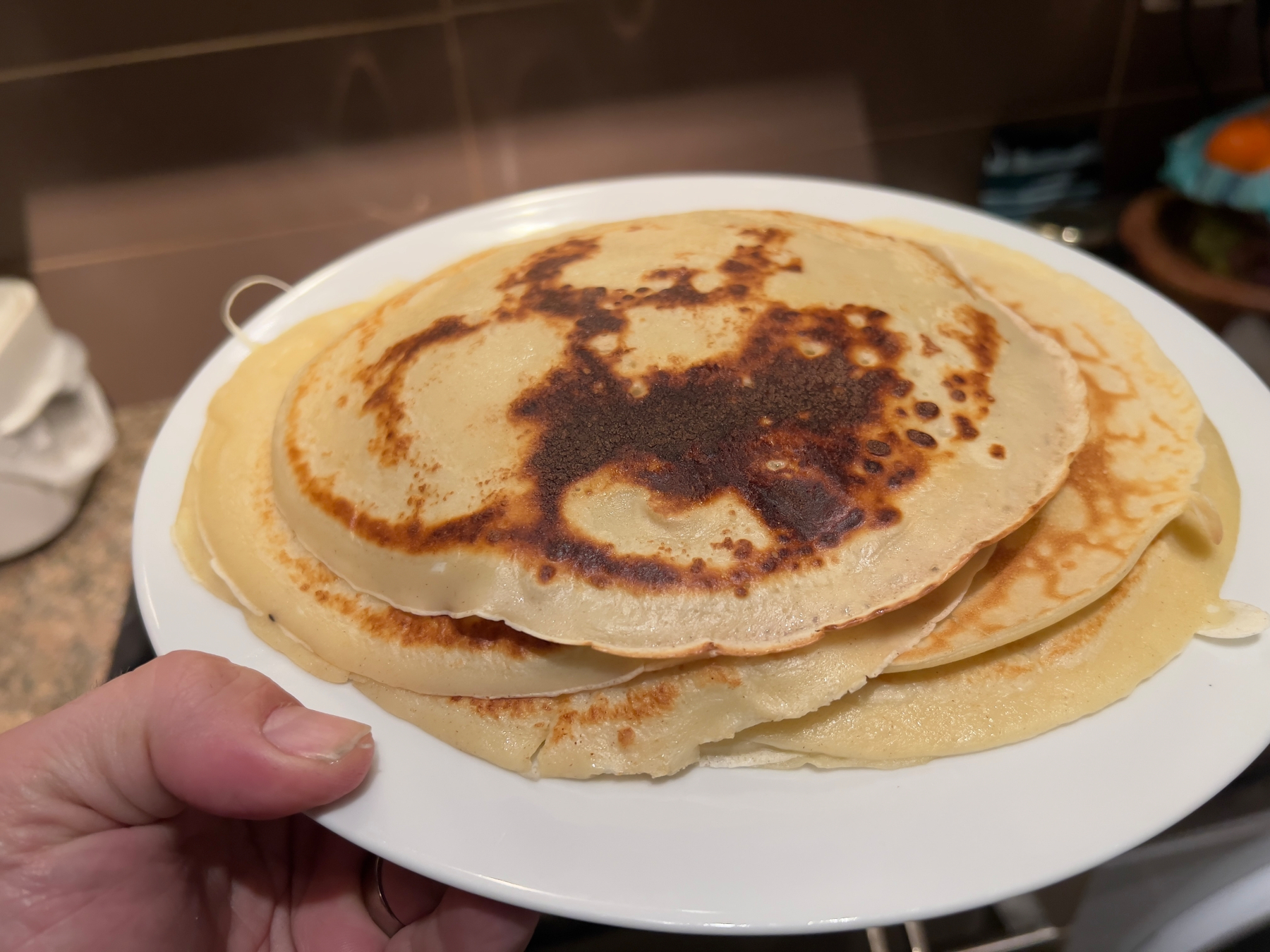 A person is holding a plate with a stack of freshly cooked crepes.