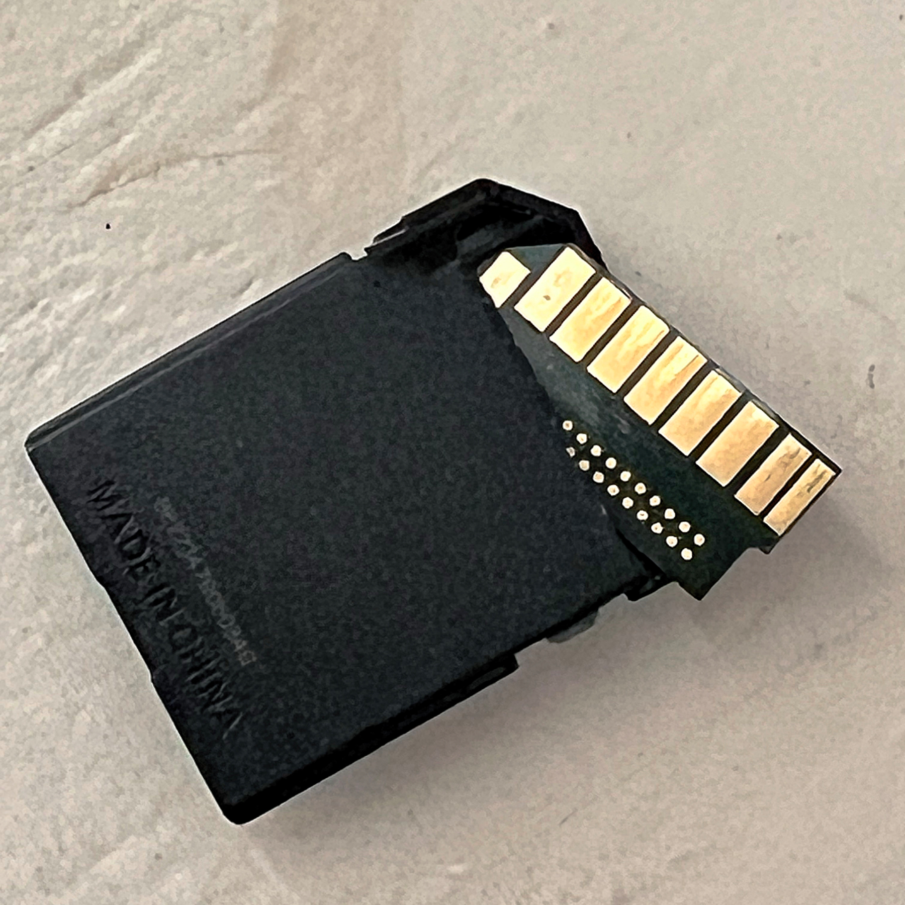 A broken black SD memory card with visible gold connectors is placed on a light-colored surface.