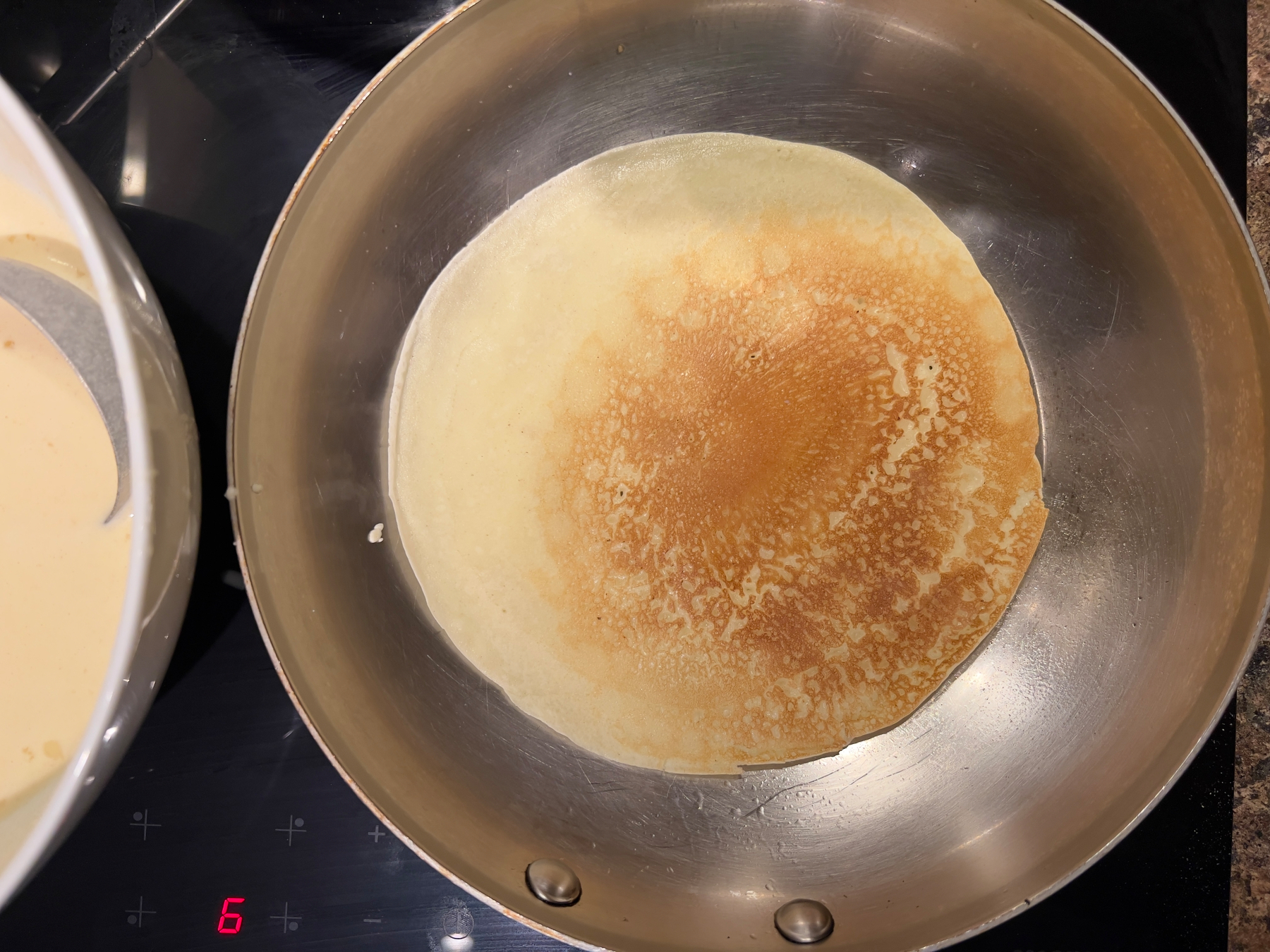 A crepe is cooking in a frying pan on an induction stove.