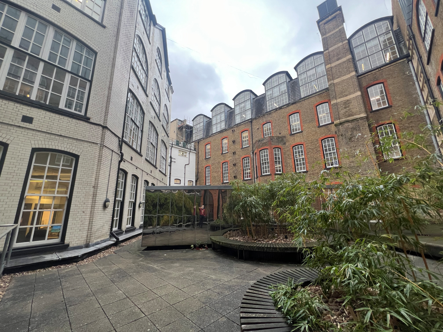 A courtyard surrounded by multistory brick and white buildings with large windows and a seating area with plants in the center.