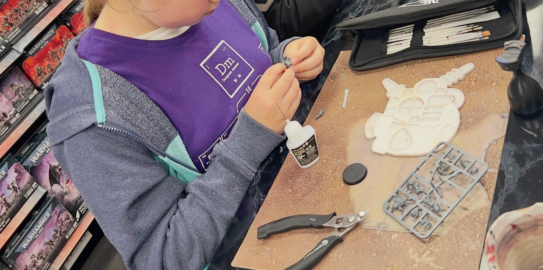 A young girl assembles a free minature of the month in a Warhammer store. 