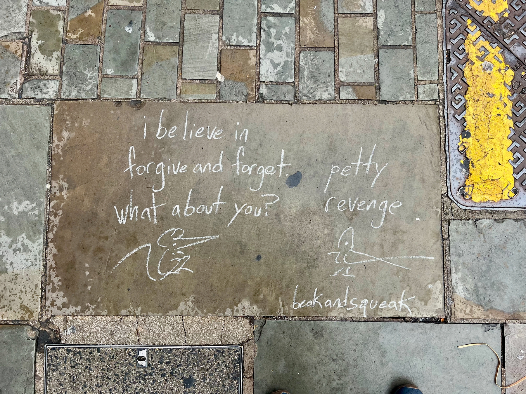 A chalk drawing on pavement shows two birds having a conversation about forgiveness versus petty revenge, signed beakandsqueak.