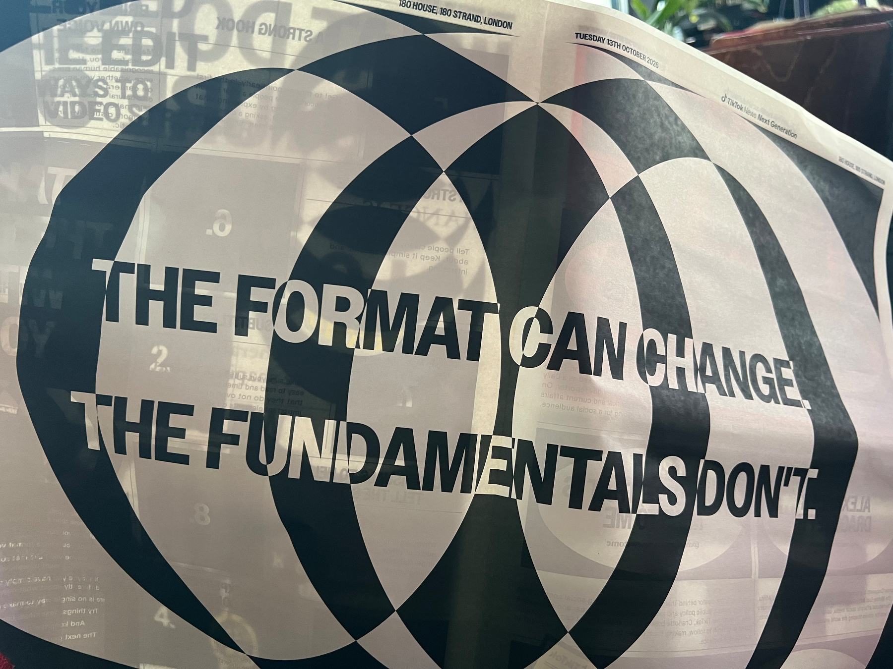 A paper held up displays the phrase THE FORMAT CAN CHANGE. THE FUNDAMENTALS DON'T. against a backdrop of overlapping black circles.