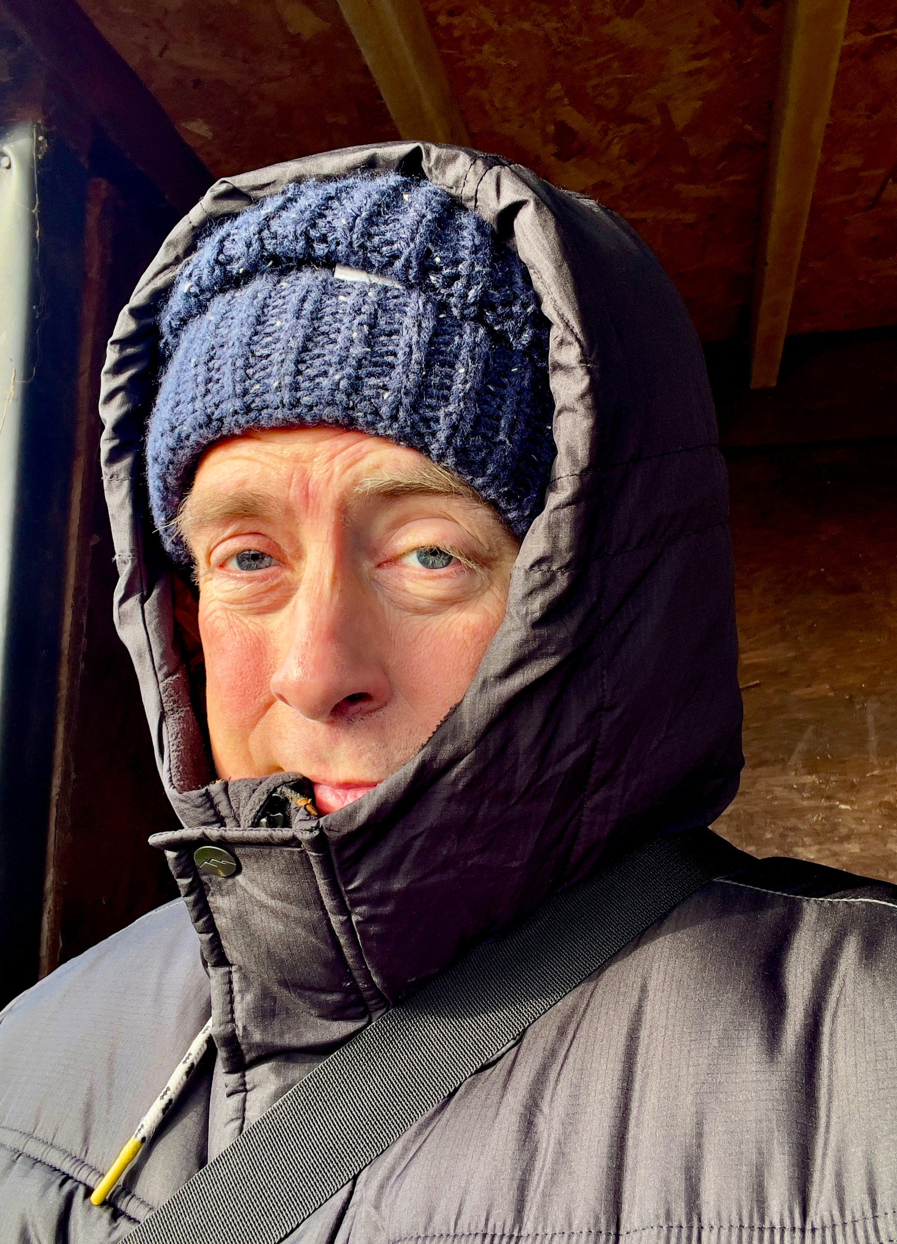 A person is bundled up in a hooded jacket and knit cap, appearing to be in a cold environment.