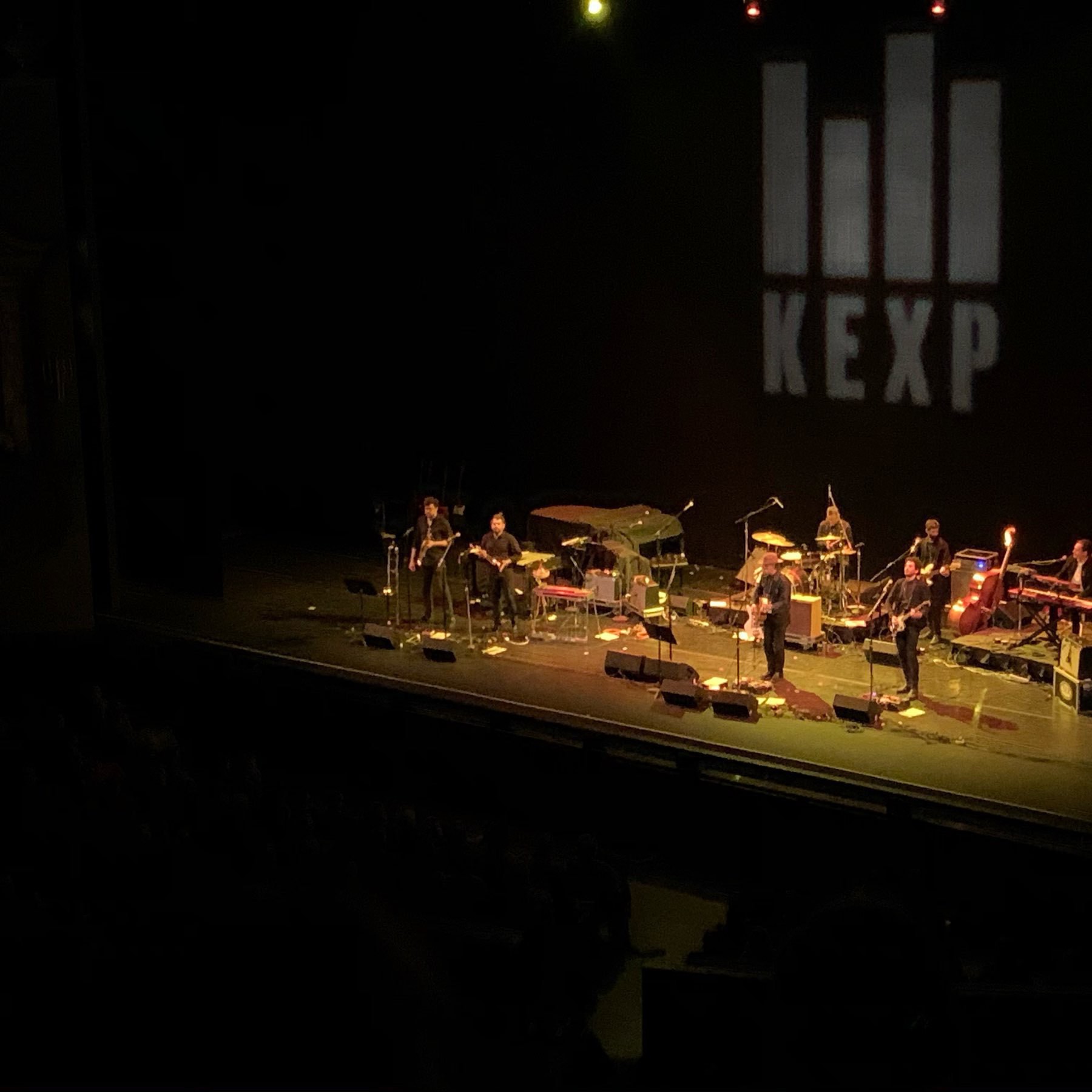 Calexico performing on stage, projected on the backdrop is the KEXP FM logo