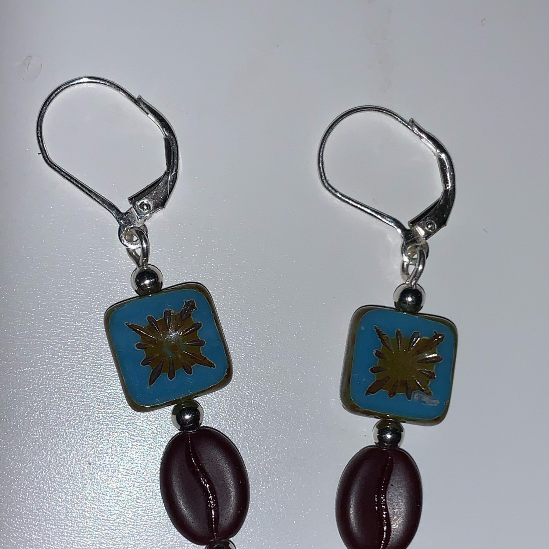 A pair of earrings each having a blue, square bead and coffee bean bead mounted on silver