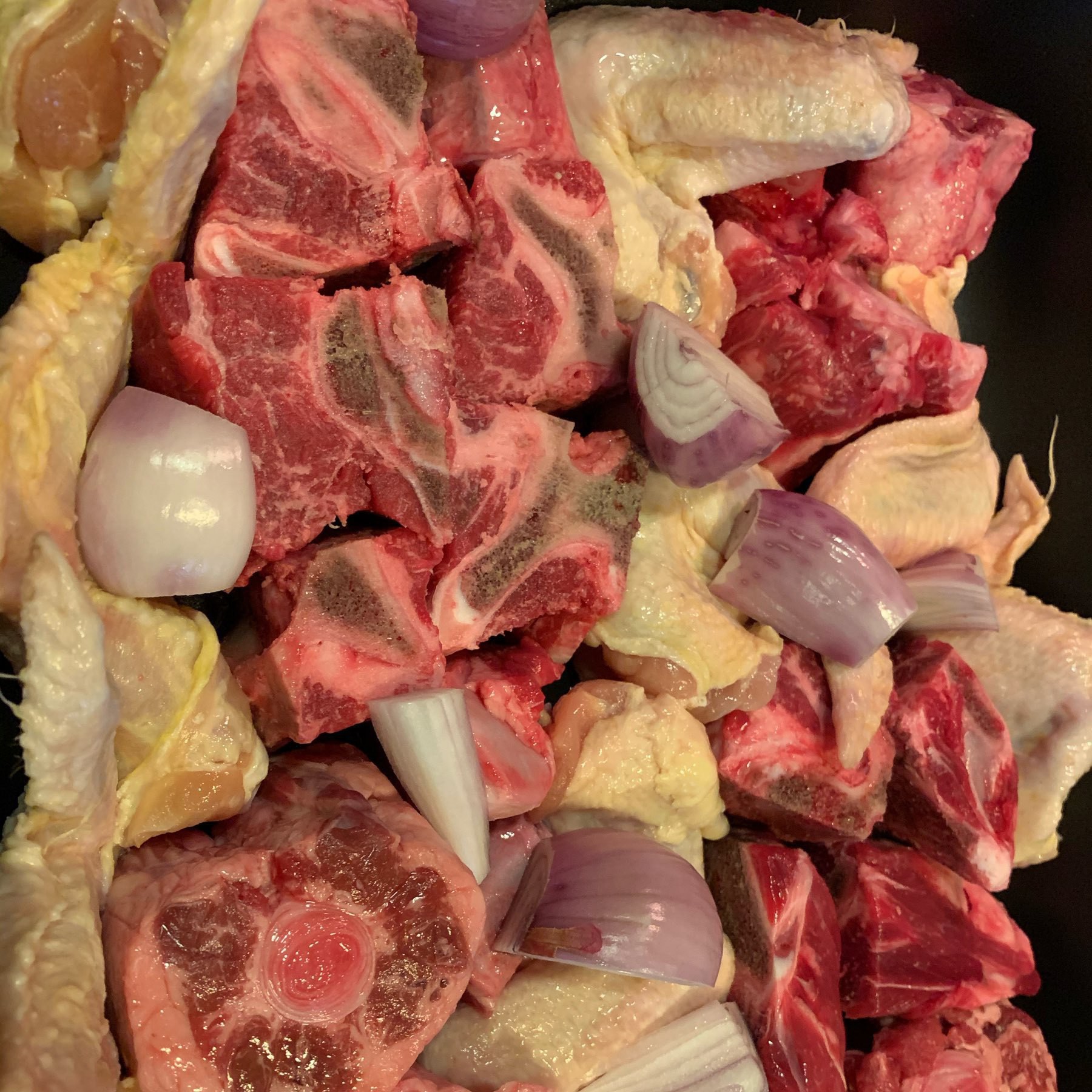 a roasting tray full of chicken wings, beef neck bones, oxtail, chicken wings, and shallots