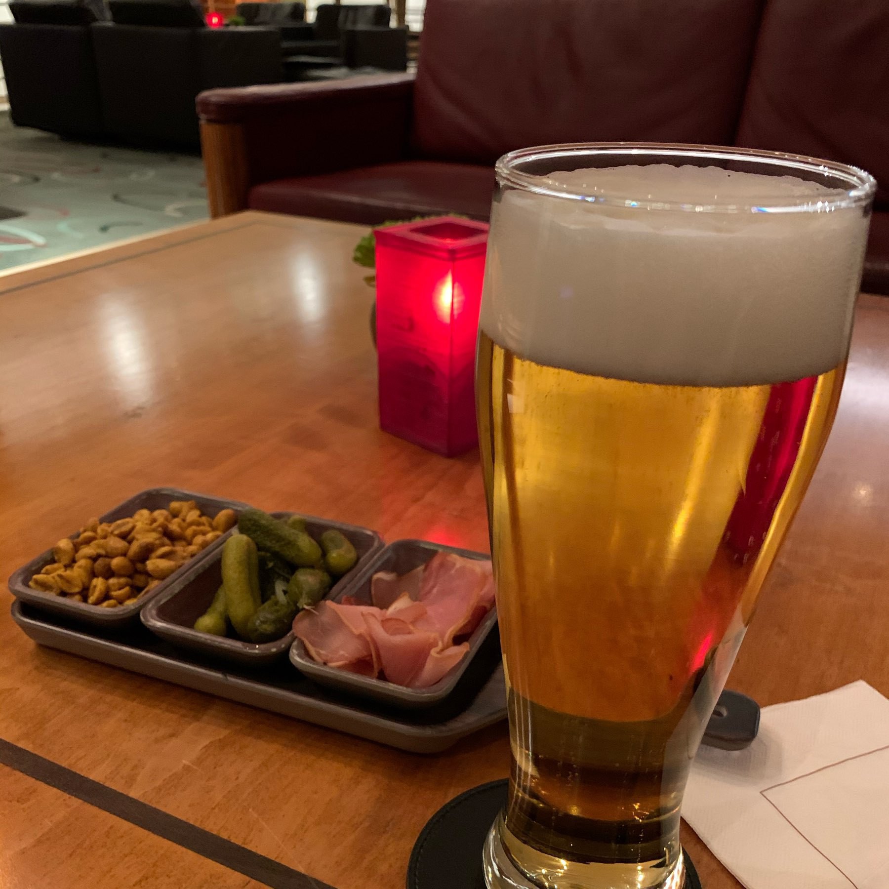 a large glass of pilsner with a tray of snacks behind it