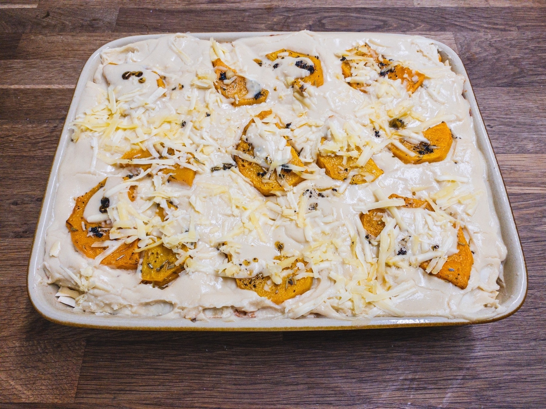 Large rectangular dish of uncooked lasagne topped with slices of butternut squash and grated cheese
