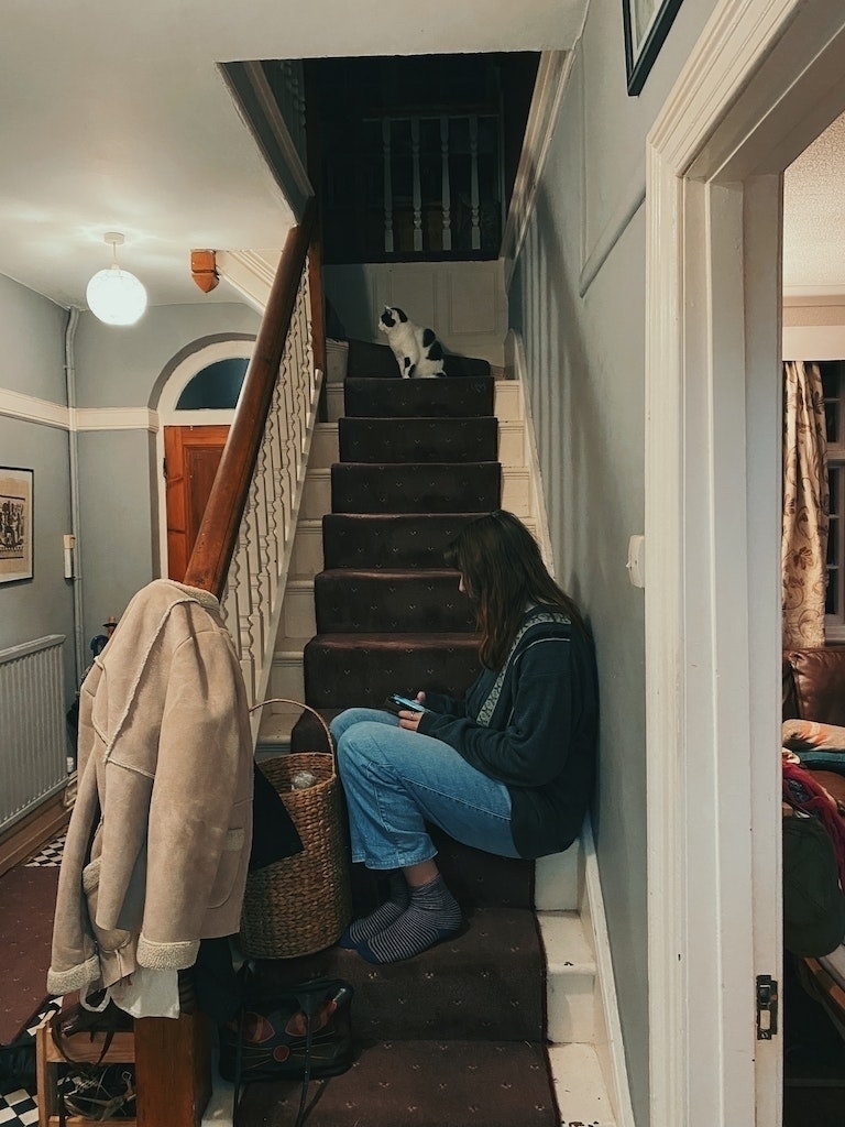 Woman using a mobile phone and black and white cat, both sitting on a flight of stairs