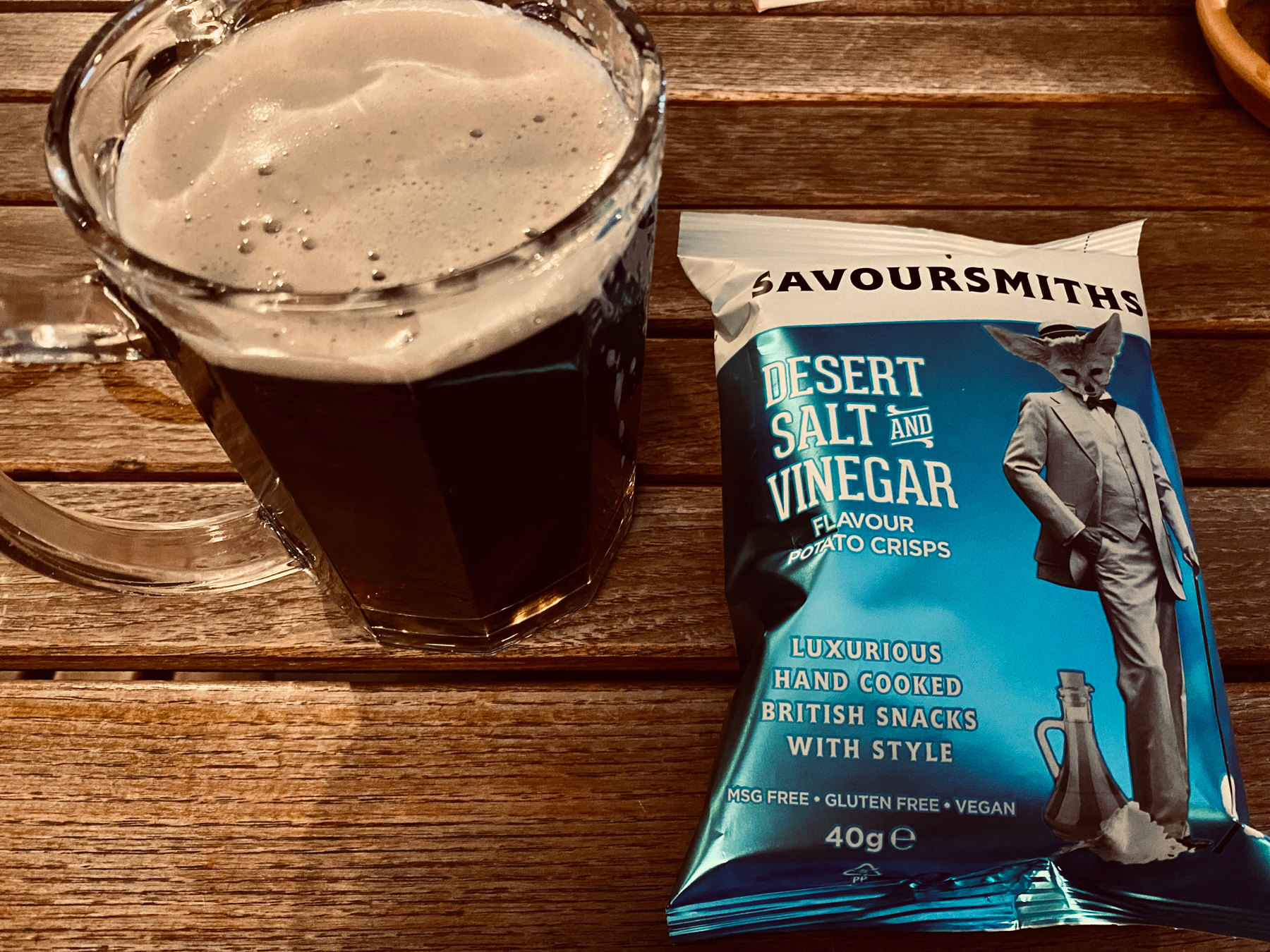 Pint glass of dark beer next to a packet of crisps