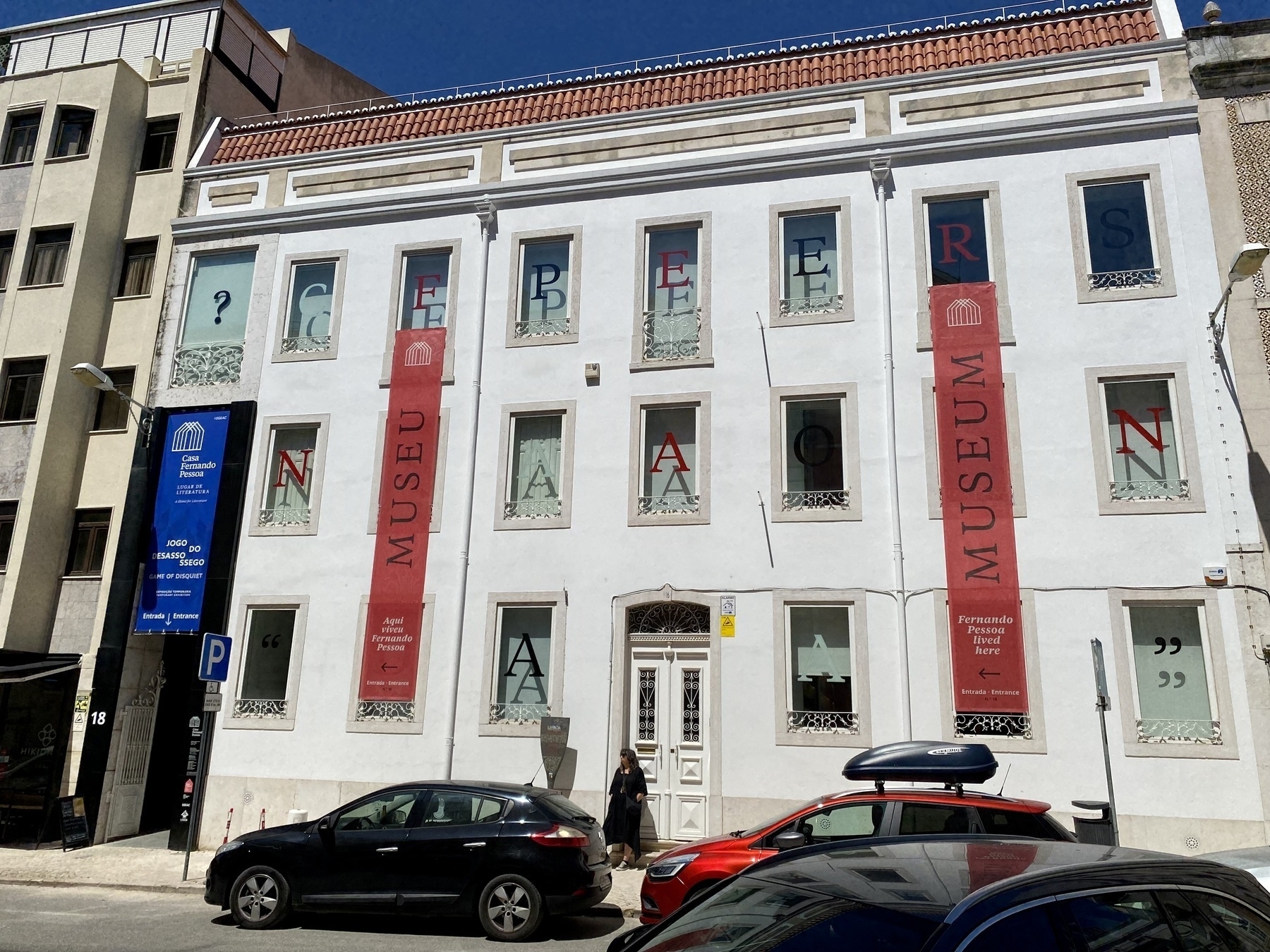 Front of plain 3-storey building, the house of Fernando Pessoa, banners labelled Museum hanging from two windows