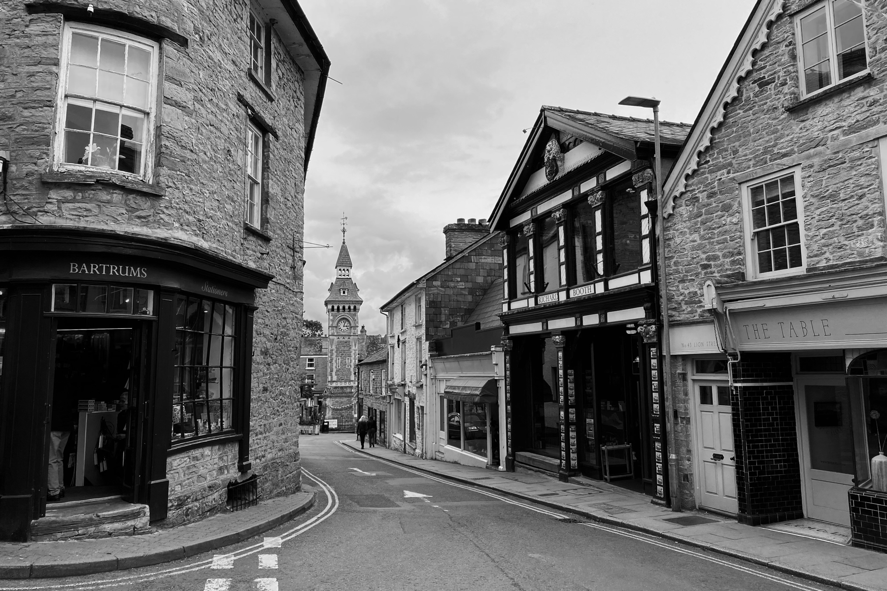Monochrome view of town street with an ornate bookshop and clock tower in the background.