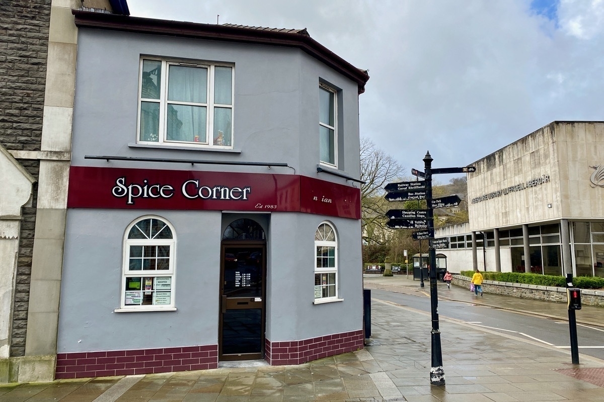 Street scene, Indian restaurant called Spice Corner in a corner house-like building next to signpost
