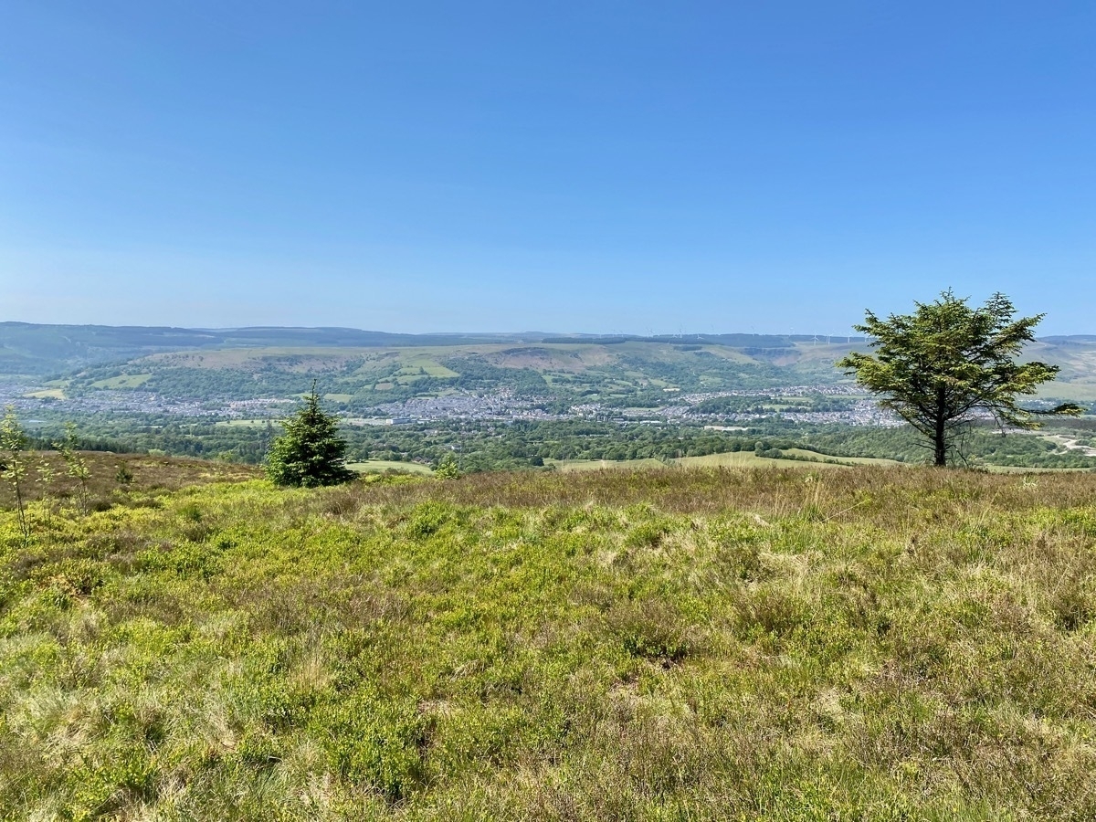 View across valley showing town below, wind turbines on distant hillside, blue skies above