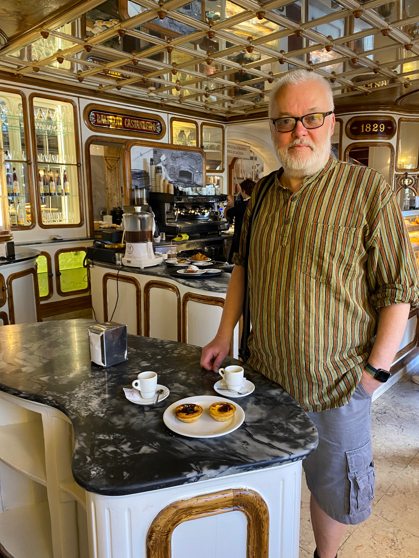 Man standing in interior of coffee shop, coffees and natas on counter in front of him