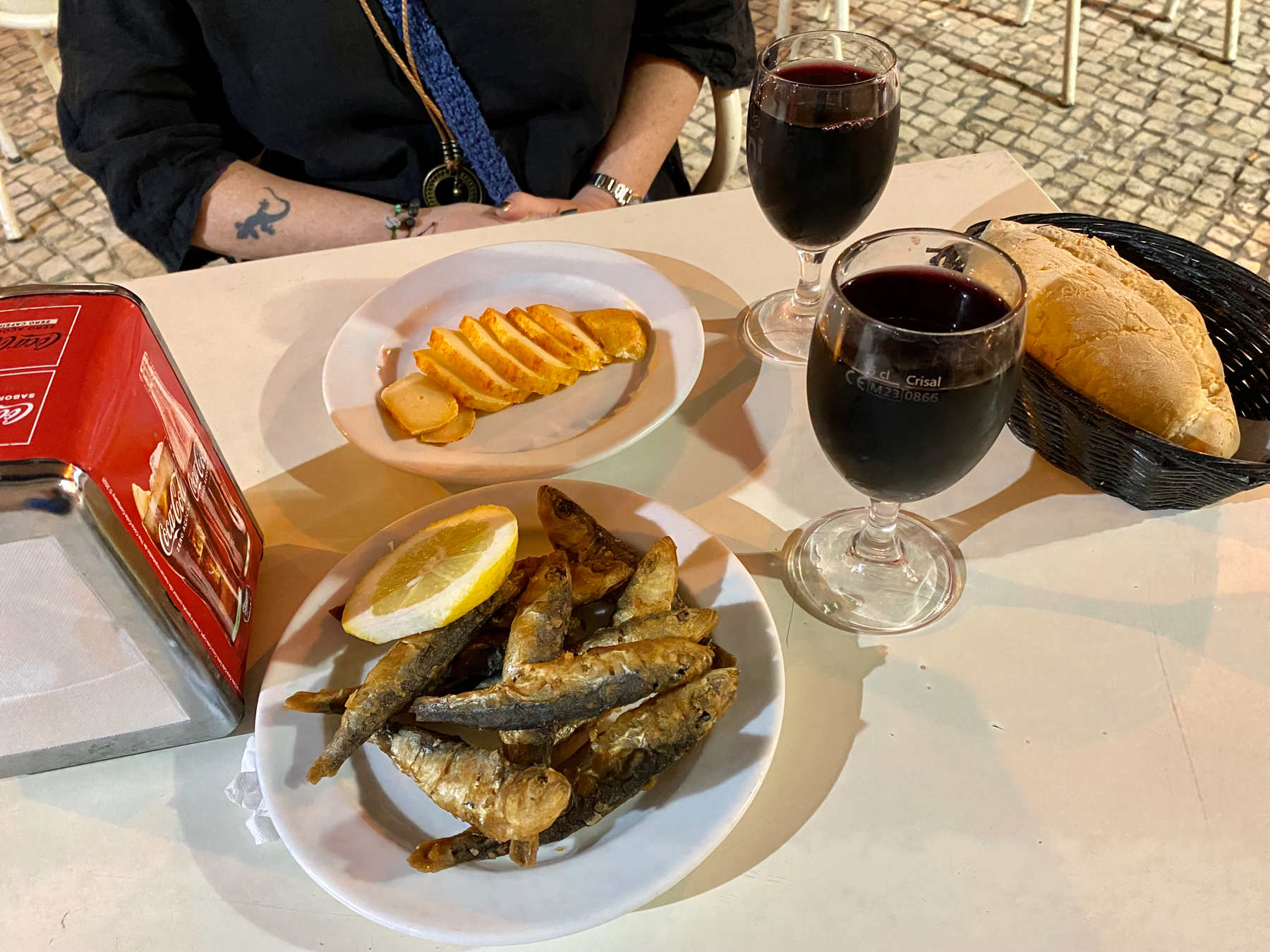 Plates of fried sardines and cheese, glasses of wine and small loaf of bread on a table