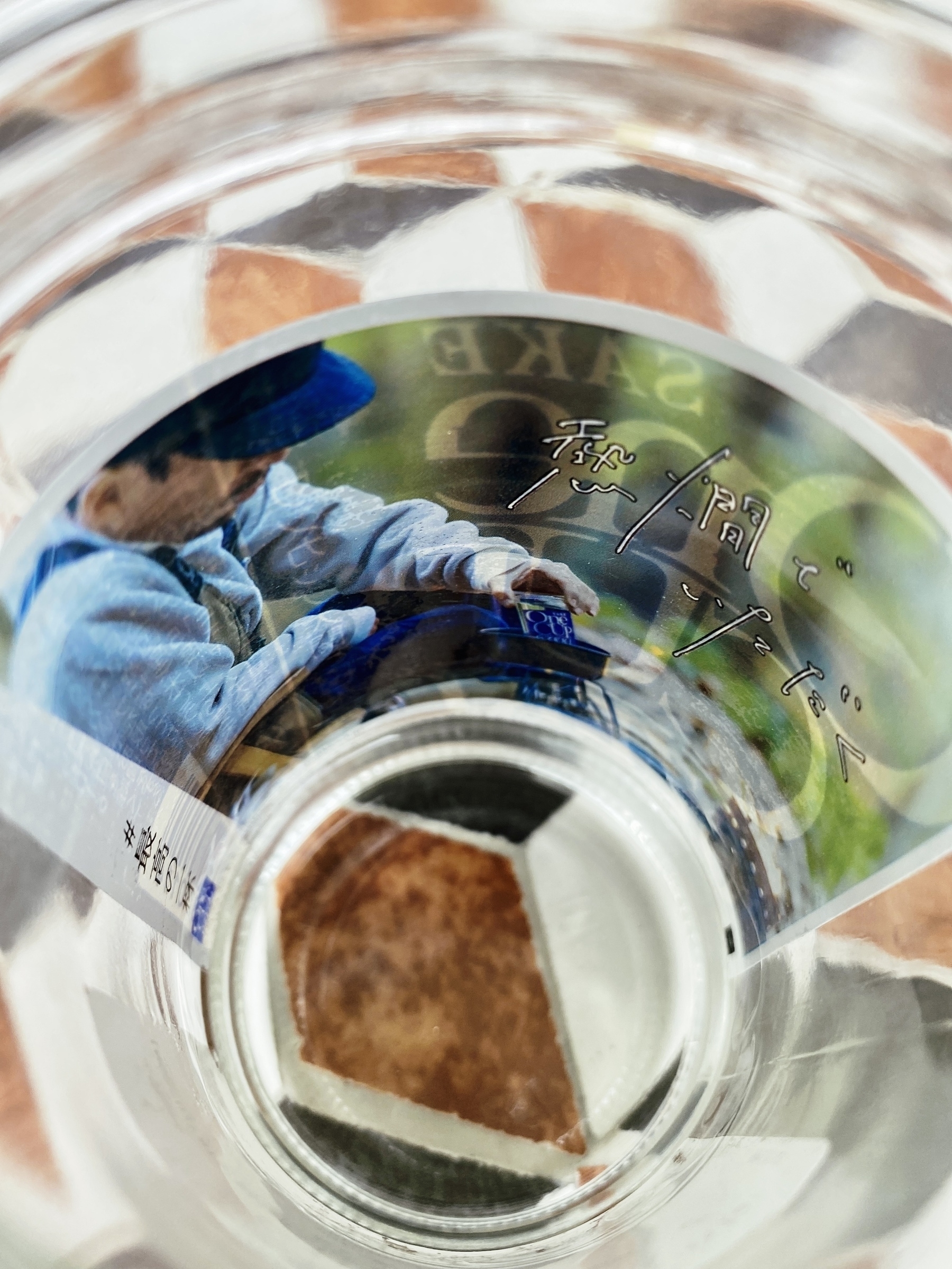 Looking down into a glass of sake with a photo sticker of a man warming sake on camping stove visible inside the glass