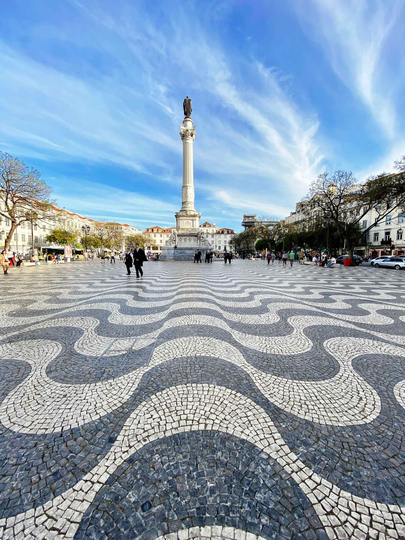 Wavy lines of balck and white mosaic tile in a town square with staue on tall column