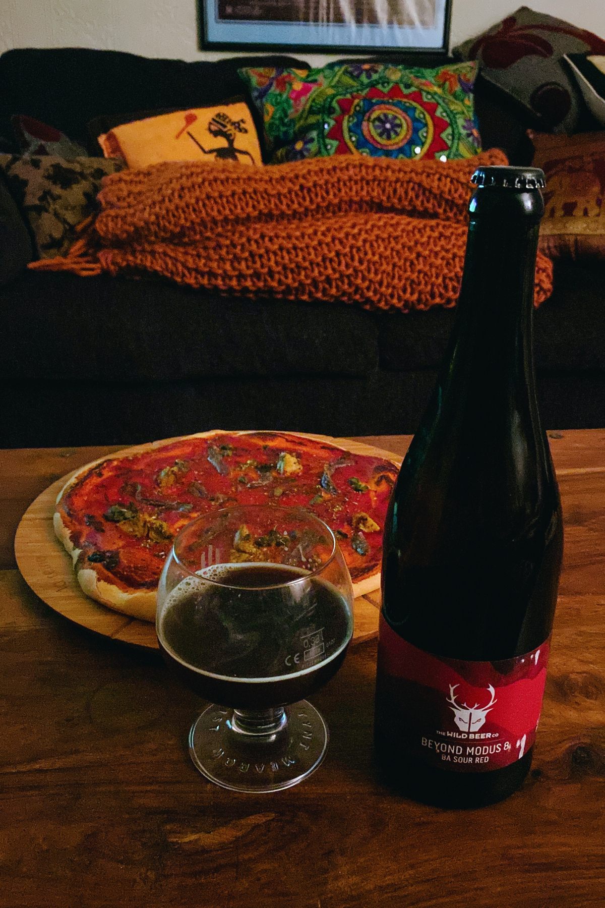 Glass and bottle of dark beer on a table in front of a pizza