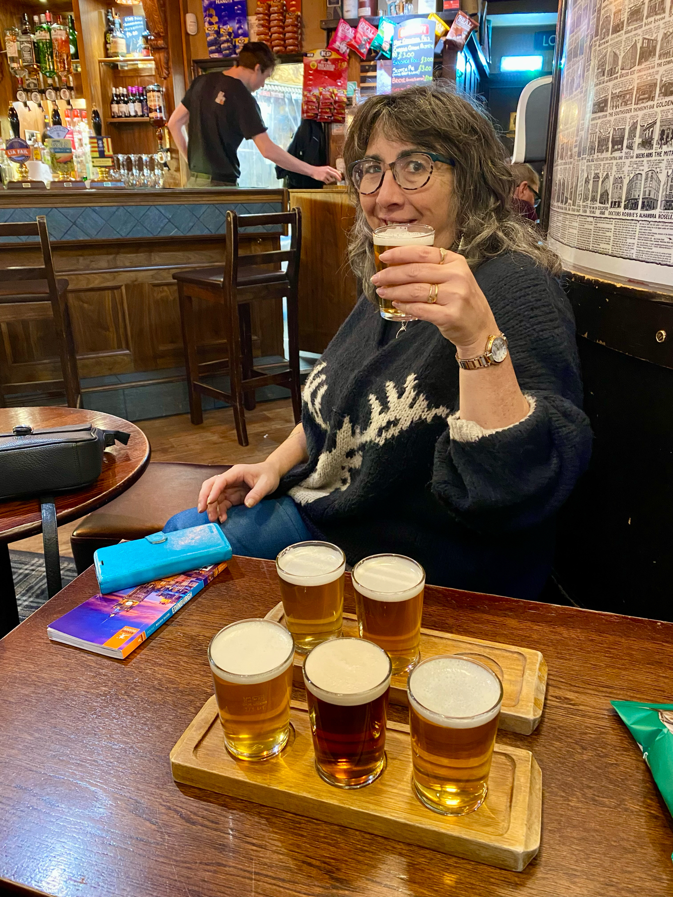 Woman sitting at a pub table with six small glasses of beer