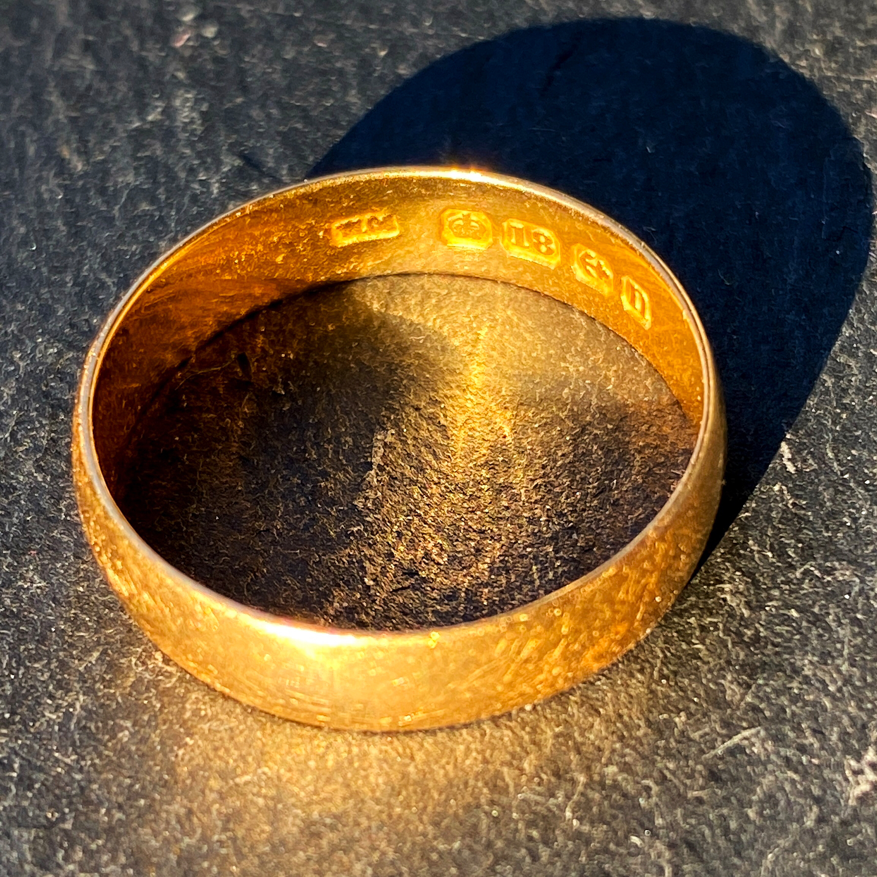 Macro photo of a gold ring on grey stone, sunlight shining on it causing reflection and shadow