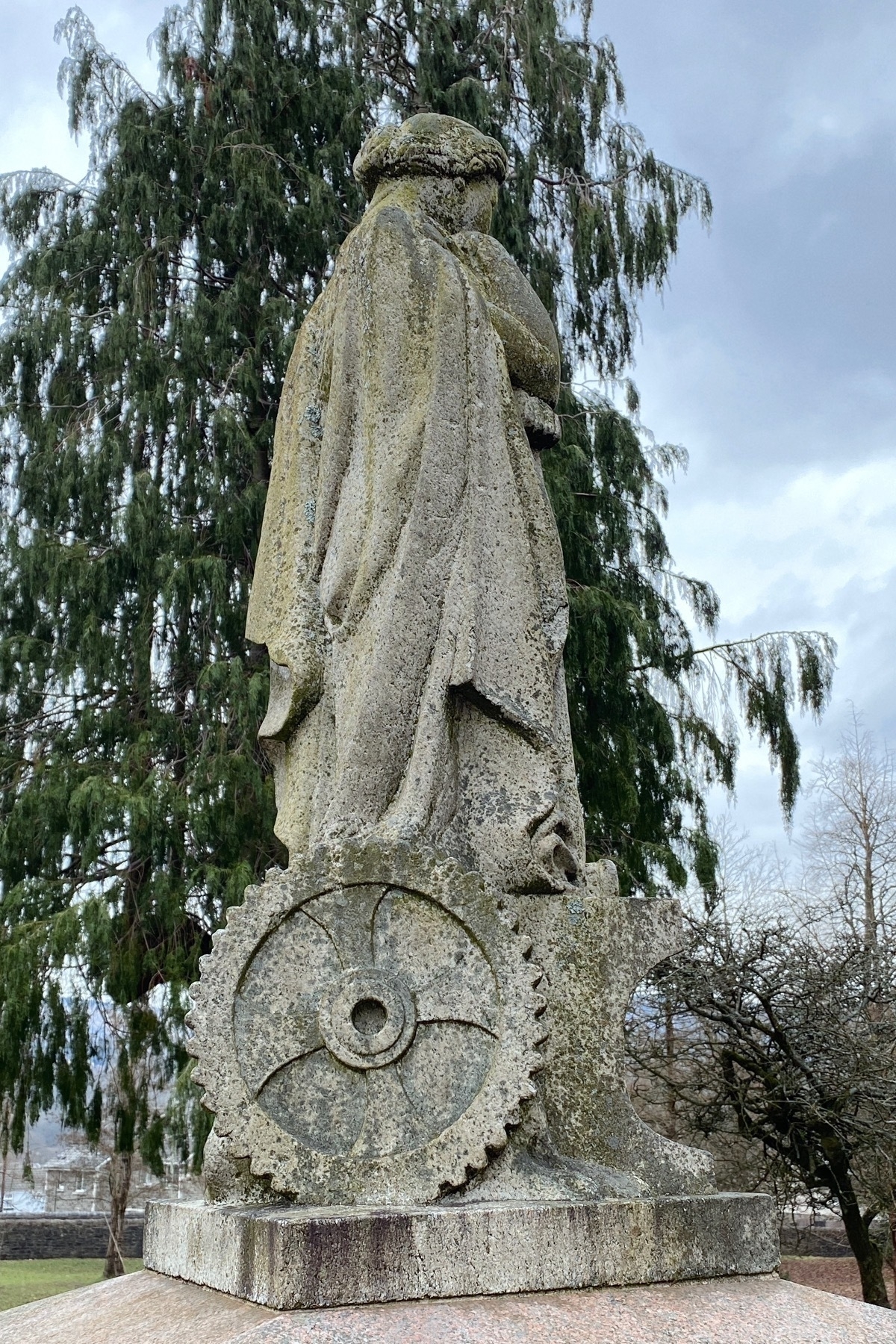 Stone statue of a woman with a cog wheel at the base