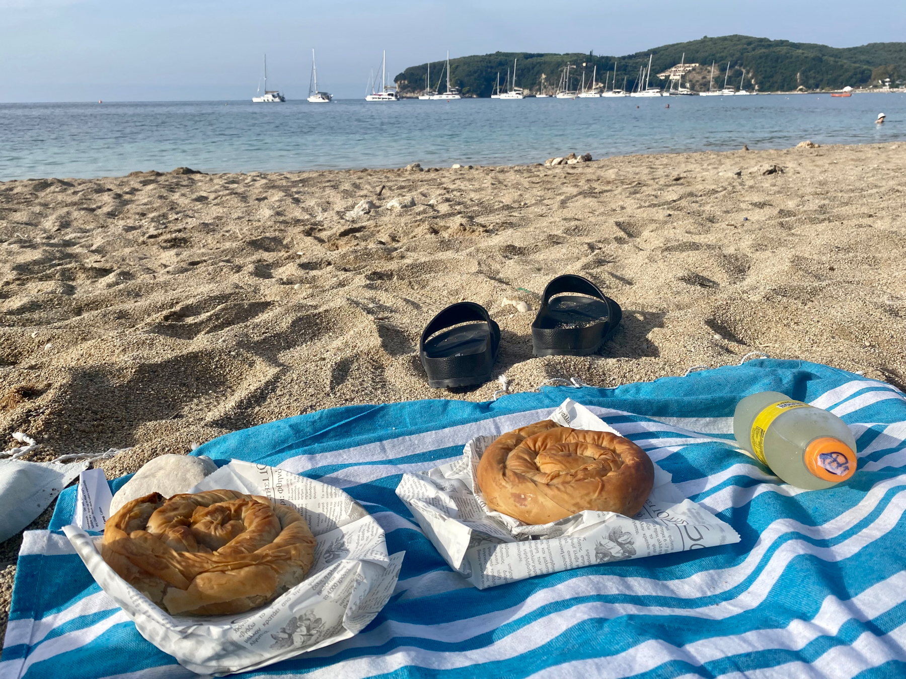 Two filo pastry pies, bottle of Fanta on a towel on a sandy beach