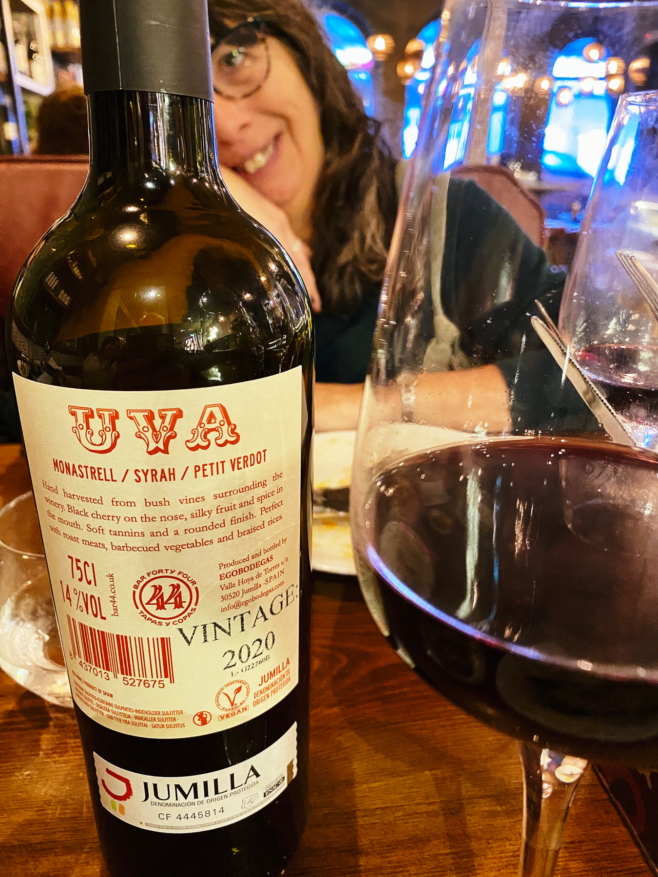 Red wine bottle and glass in foreground, smiling woman in background