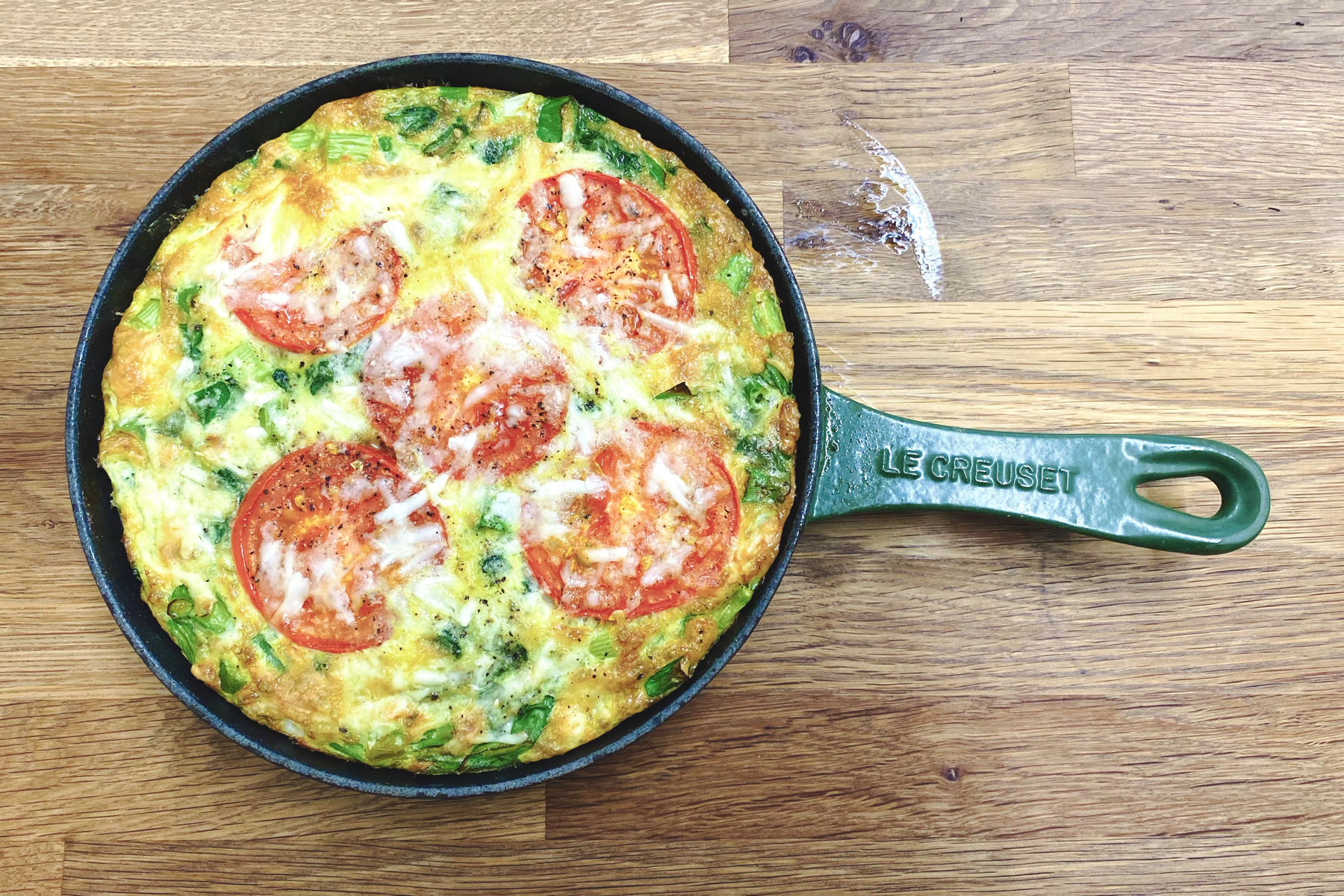 Overhead view of tomato topped frittata in green Le Creuset frying pan